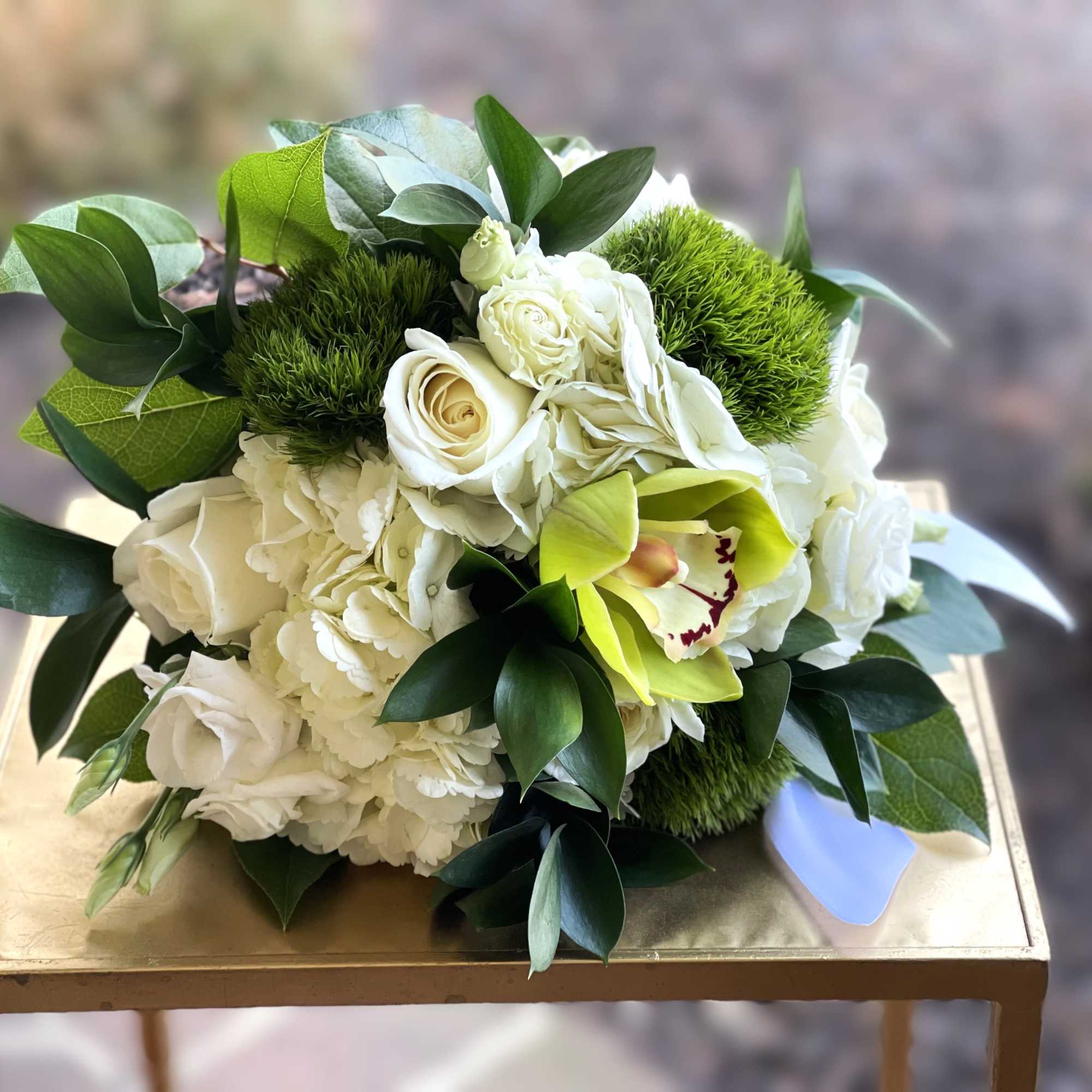 Compact bouquet of white roses and hydrangeas with a green cymbidium orchid accent