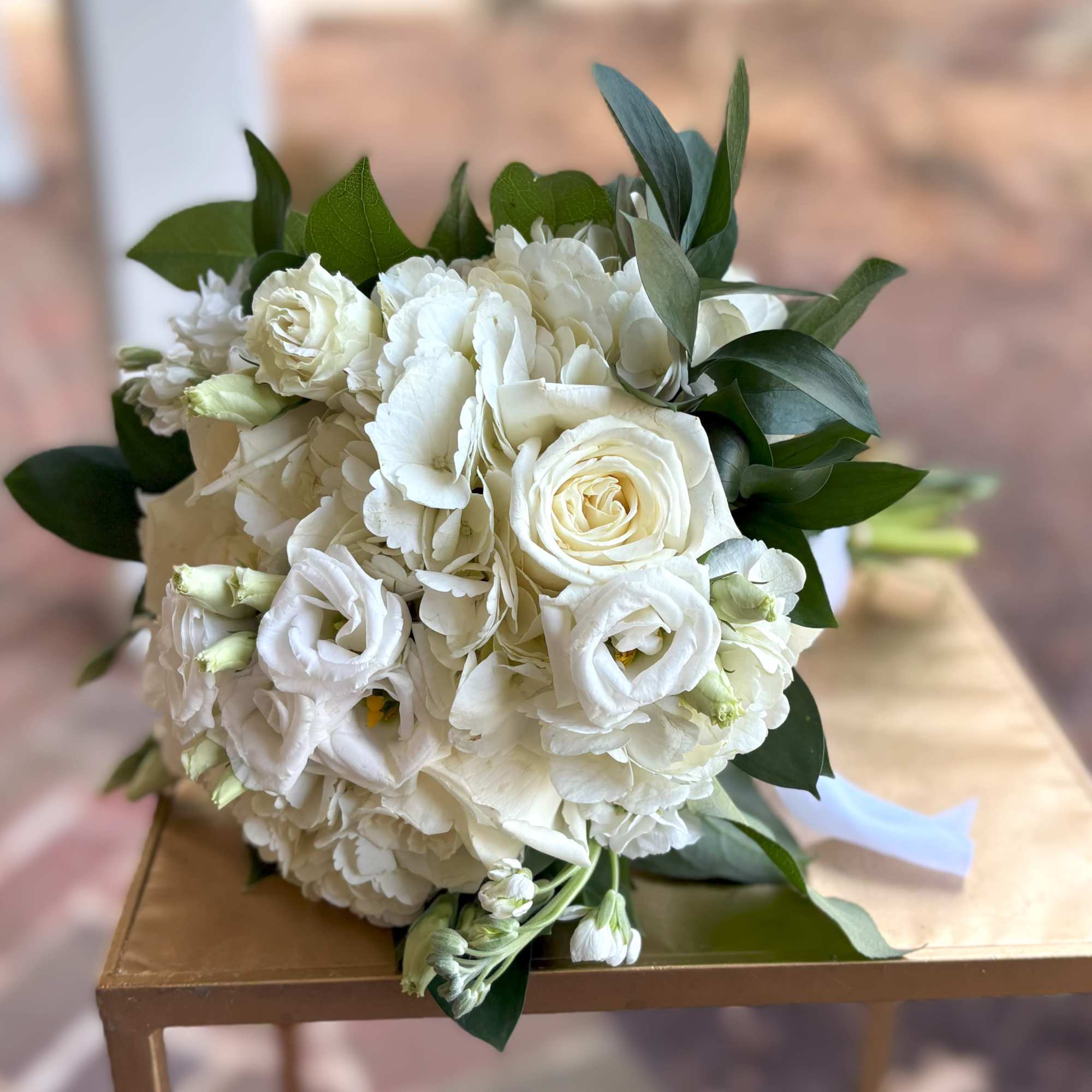 Round bouquet of white roses and hydrangeas with buds and greenery, resting on a small table