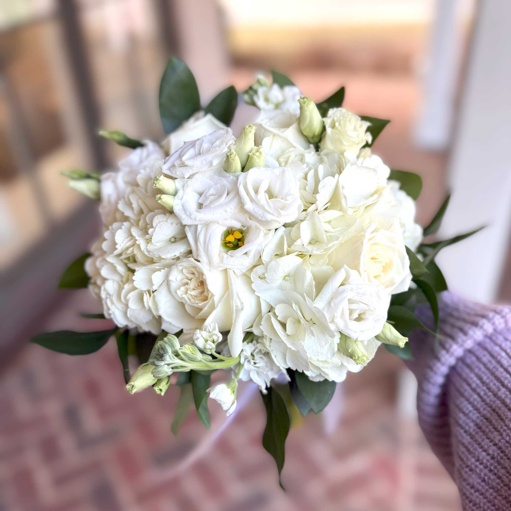 Hand-tied bouquet of white roses, lisianthus, and hydrangea with dark green accents