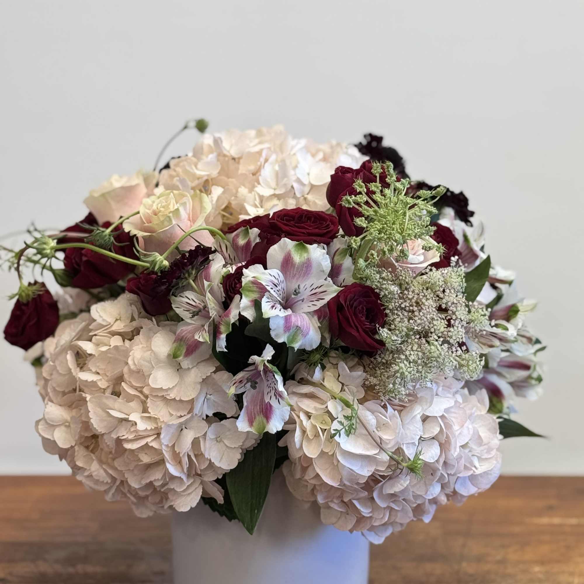 Bouquet of pale hydrangeas and burgundy roses in a white vase