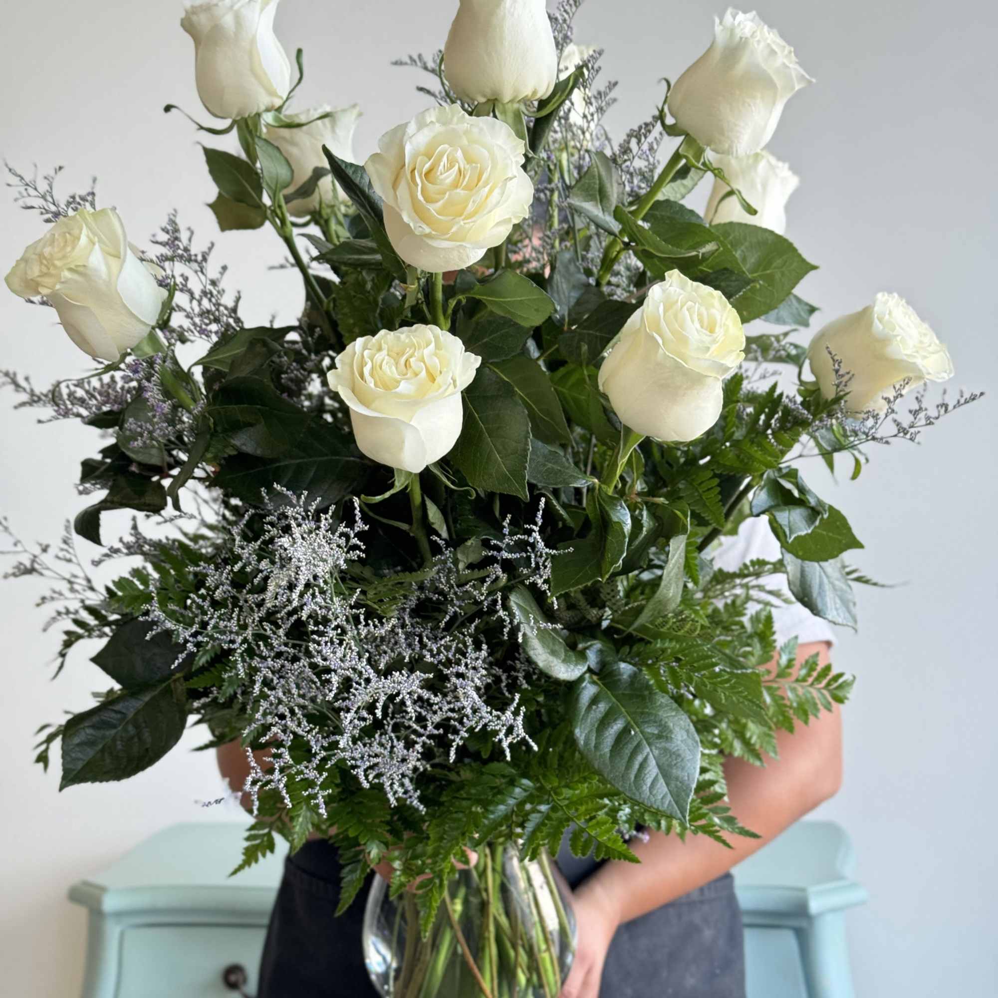 White roses arranged in a clear glass vase with greenery
