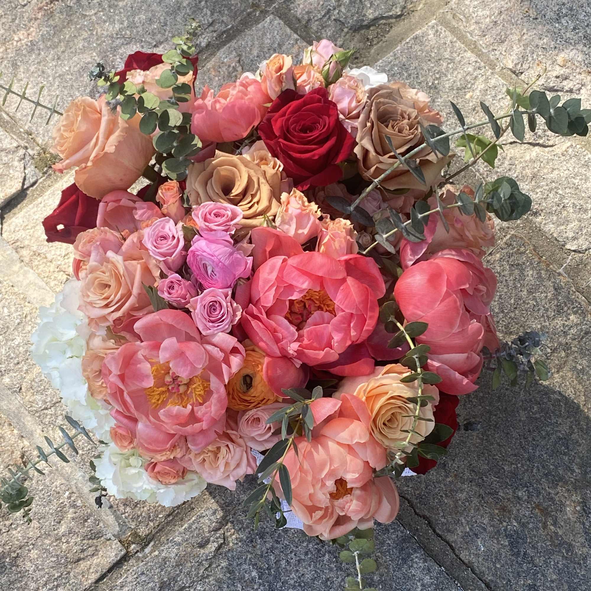 Round bouquet of pink, peach, and red flowers with eucalyptus