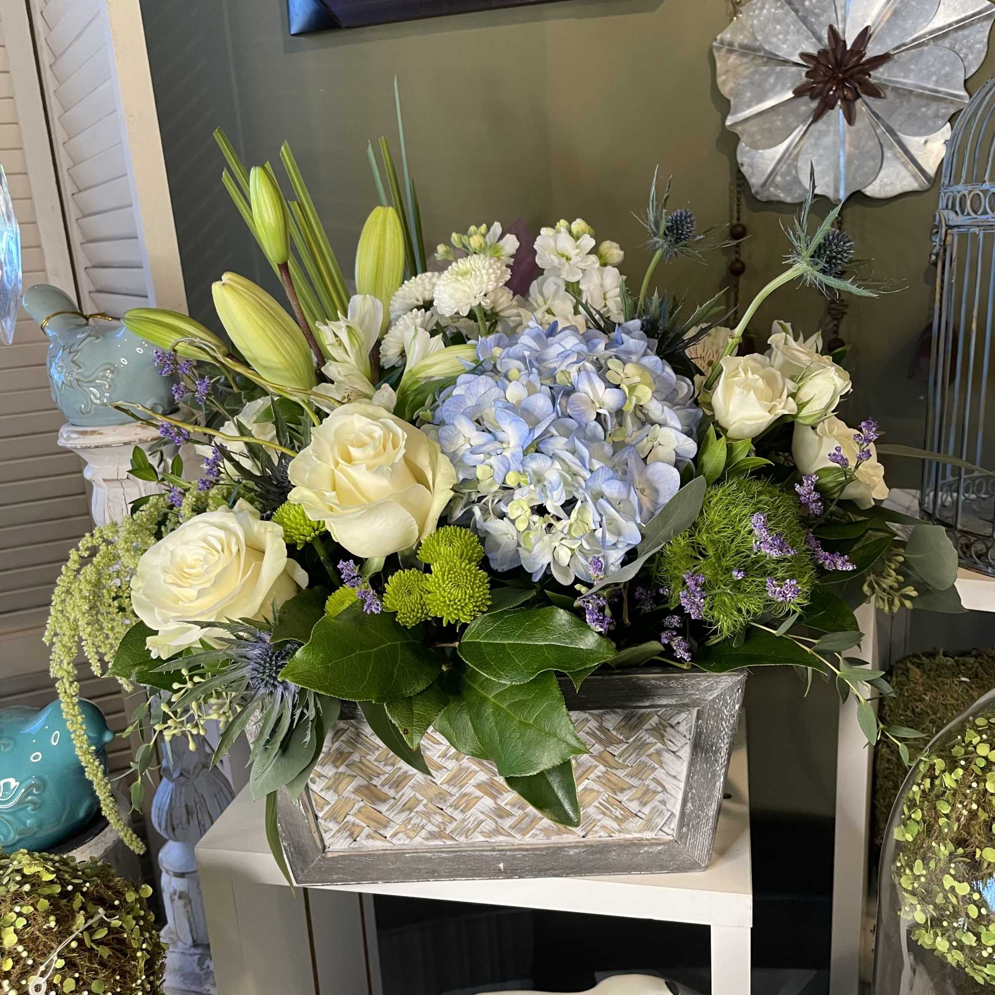 Large floral arrangement with white roses, blue hydrangea, and lilies in a rectangular container