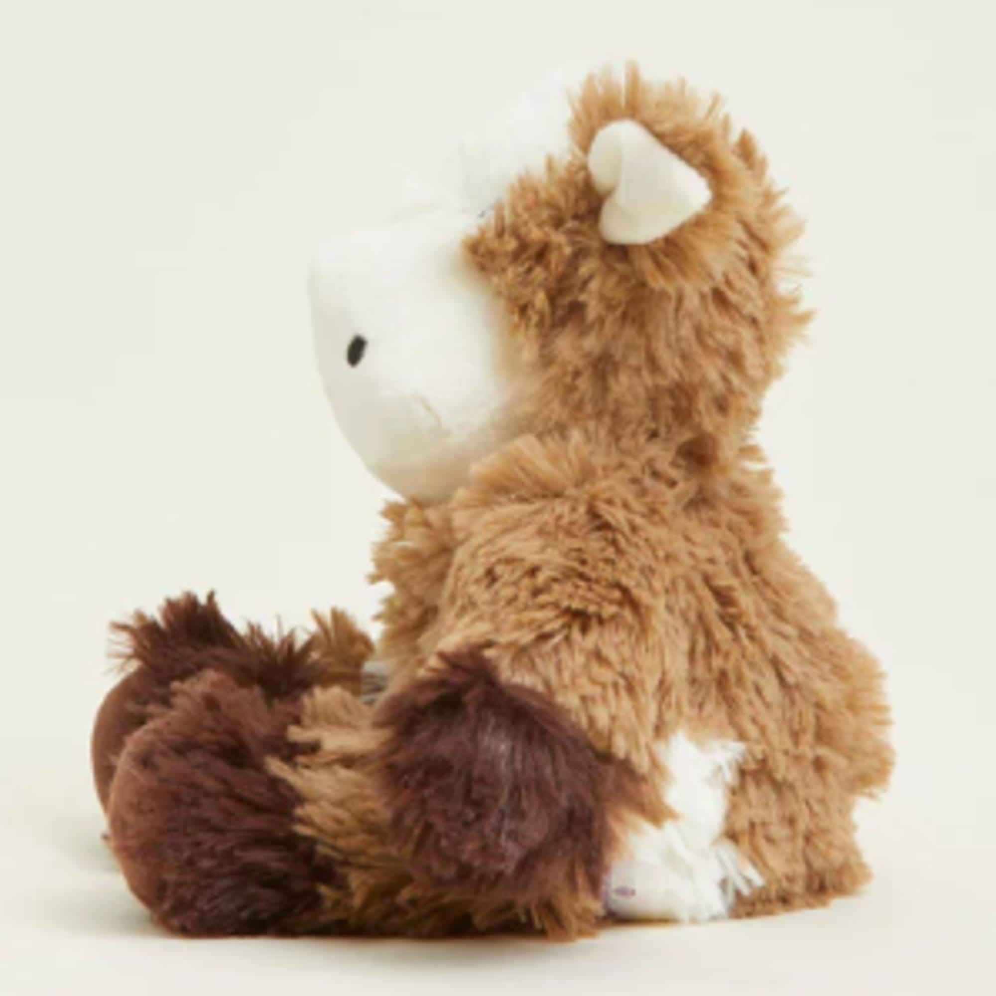 Brown plush teddy bear sitting in profile on a light background