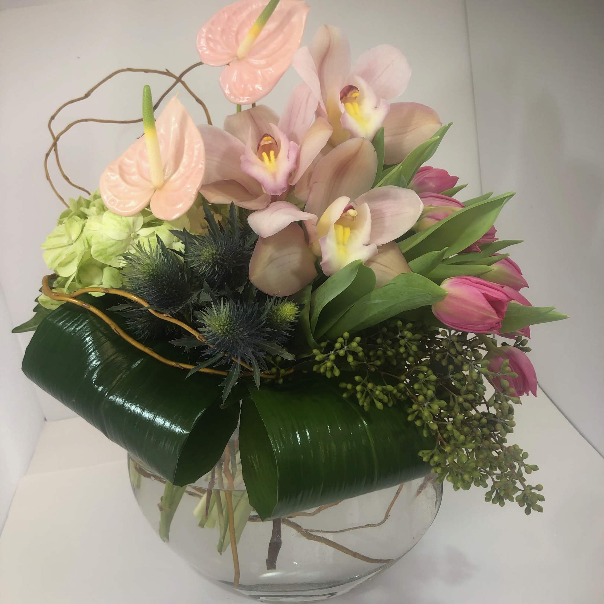 Pink orchids and anthuriums arranged in a clear glass bowl
