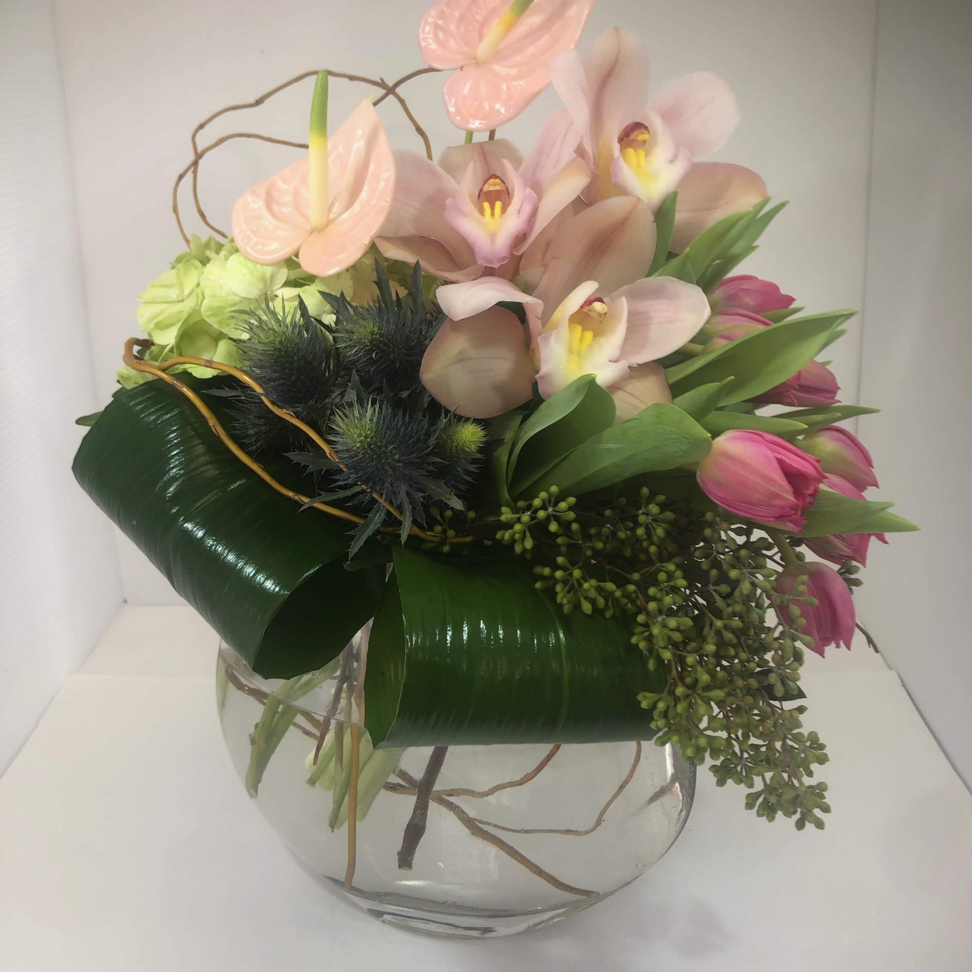 Pink orchids and tulips arranged in a clear glass vase