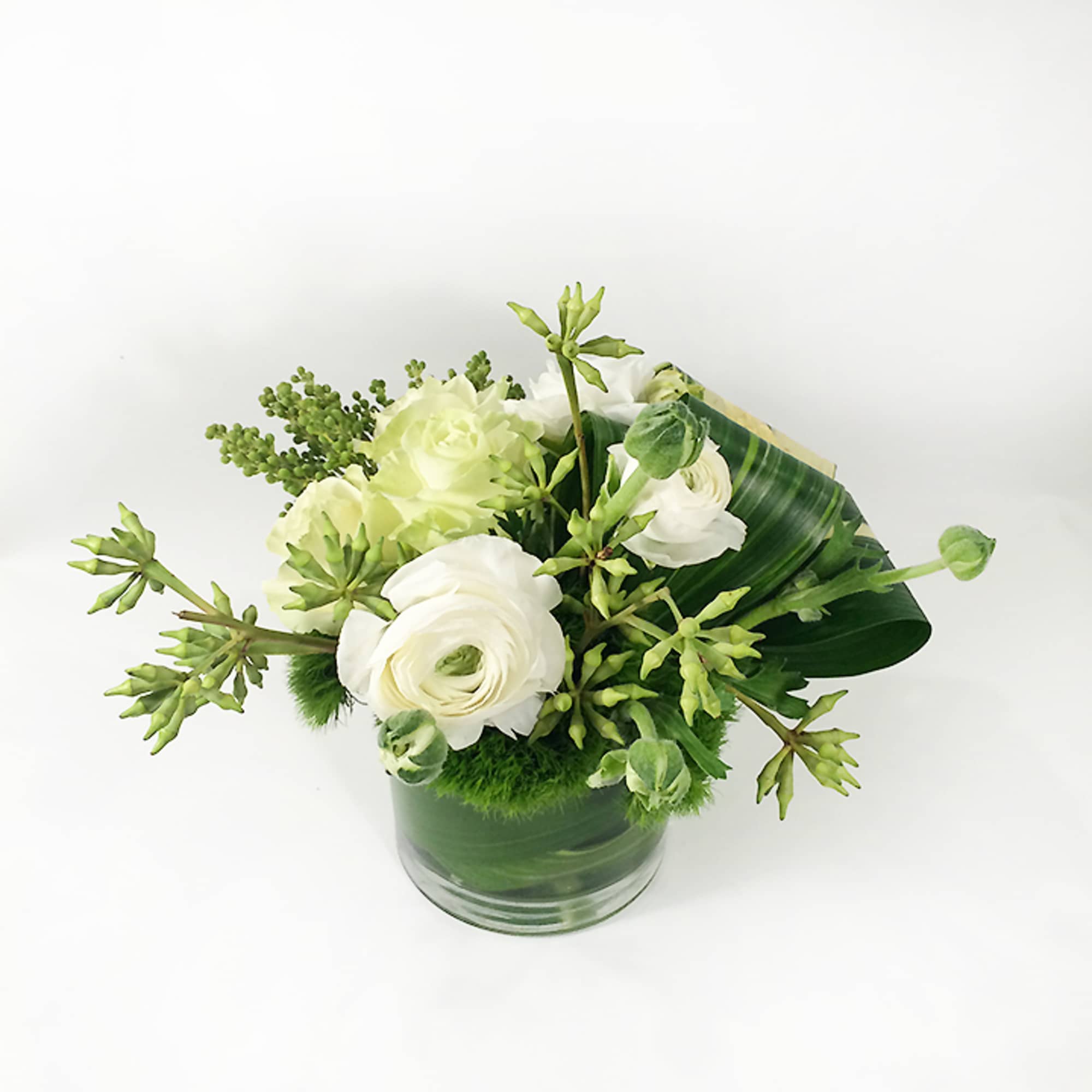White flowers arranged in a green glass vase with broad leaves