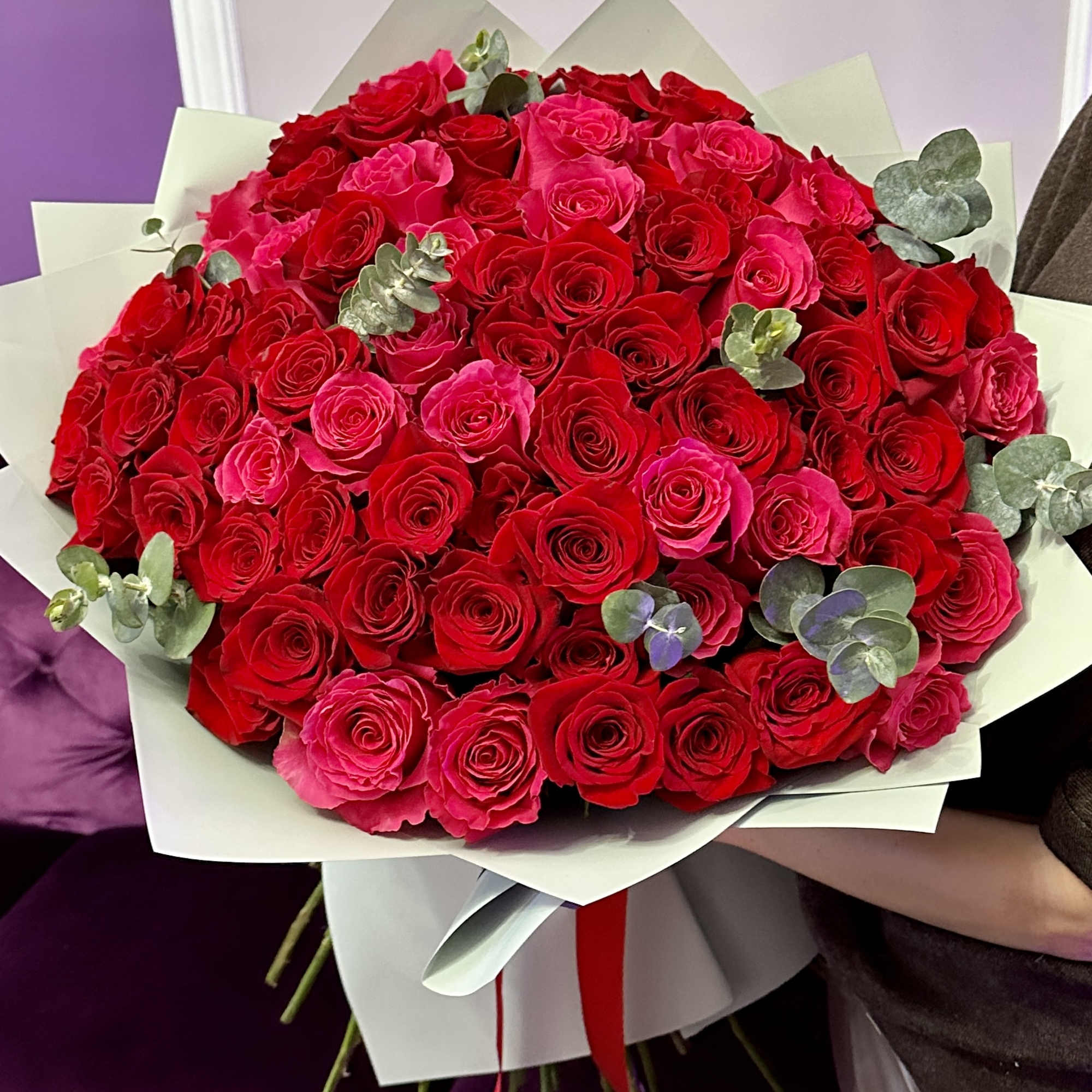 Large hand-tied bouquet of red and hot pink roses with eucalyptus wrapped in white paper