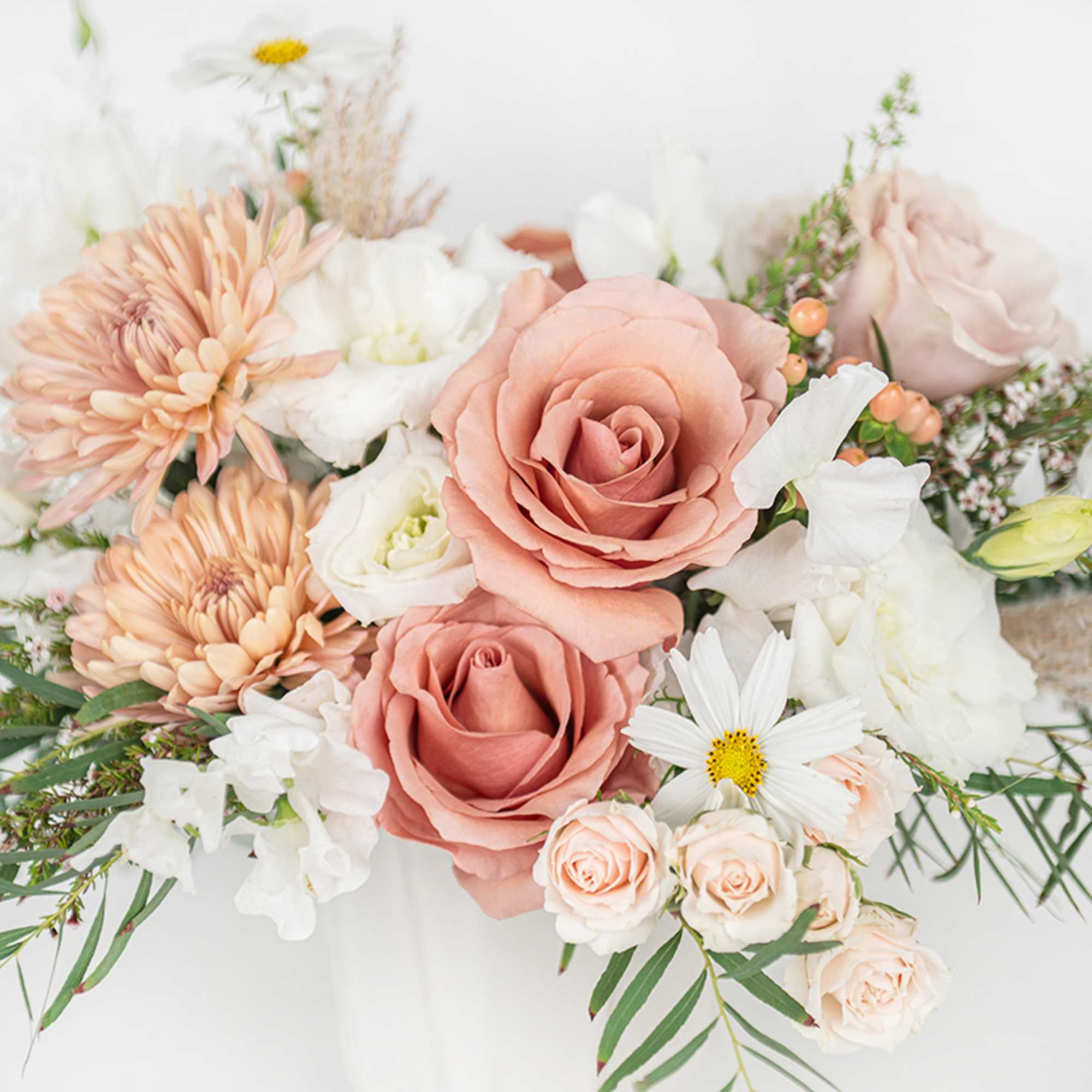 Peach roses, white blooms, and soft peach chrysanthemums arranged in a light, airy bouquet