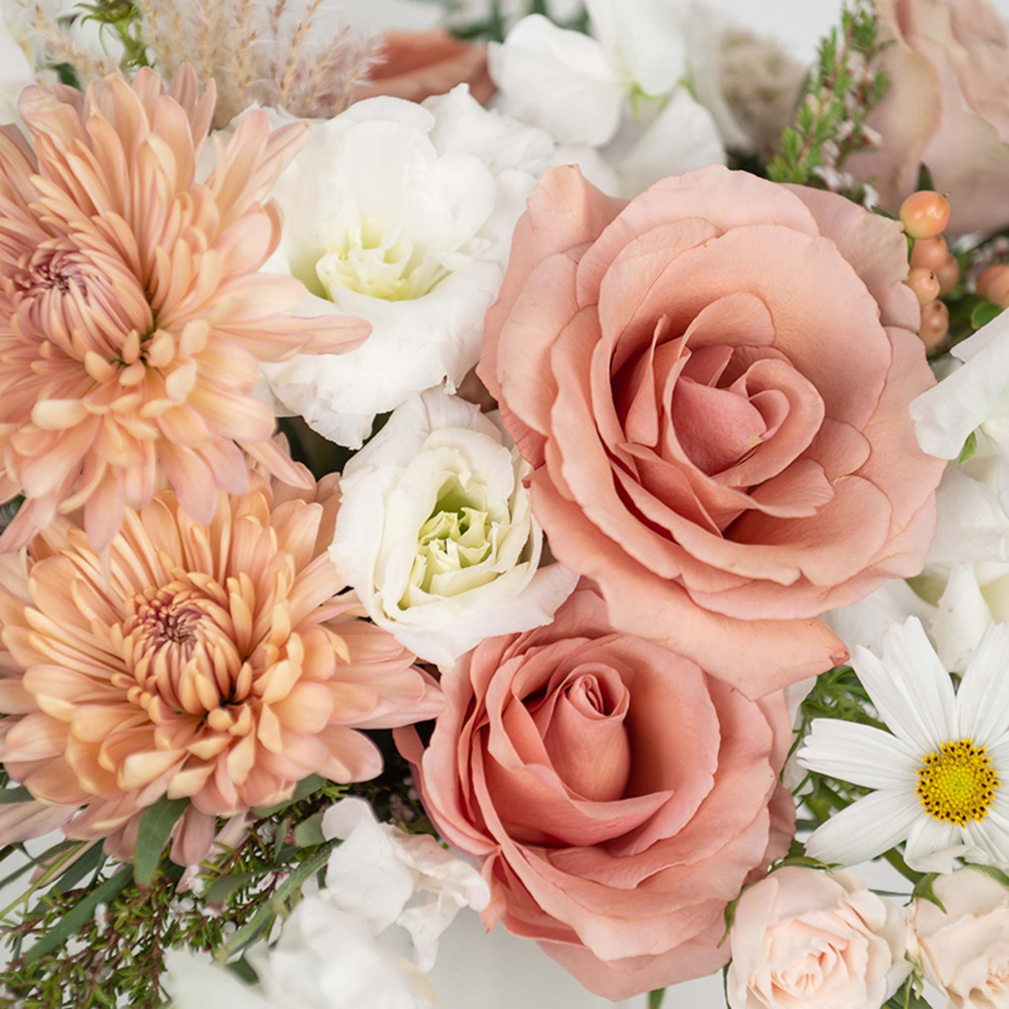 Close-up of peach roses, mums, and white blooms in a soft pastel arrangement