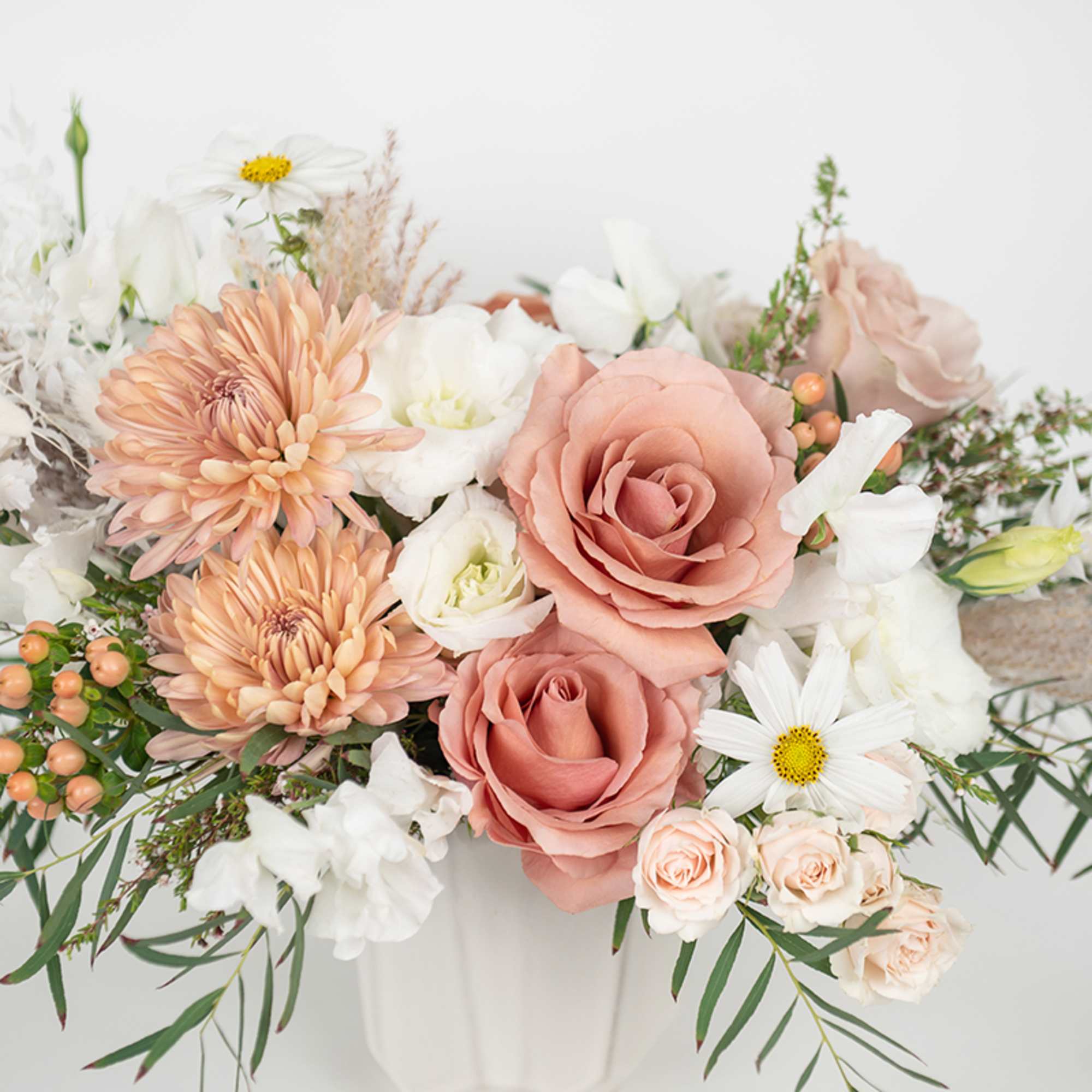 Peach roses and chrysanthemums mixed with white blooms in a white ceramic vase