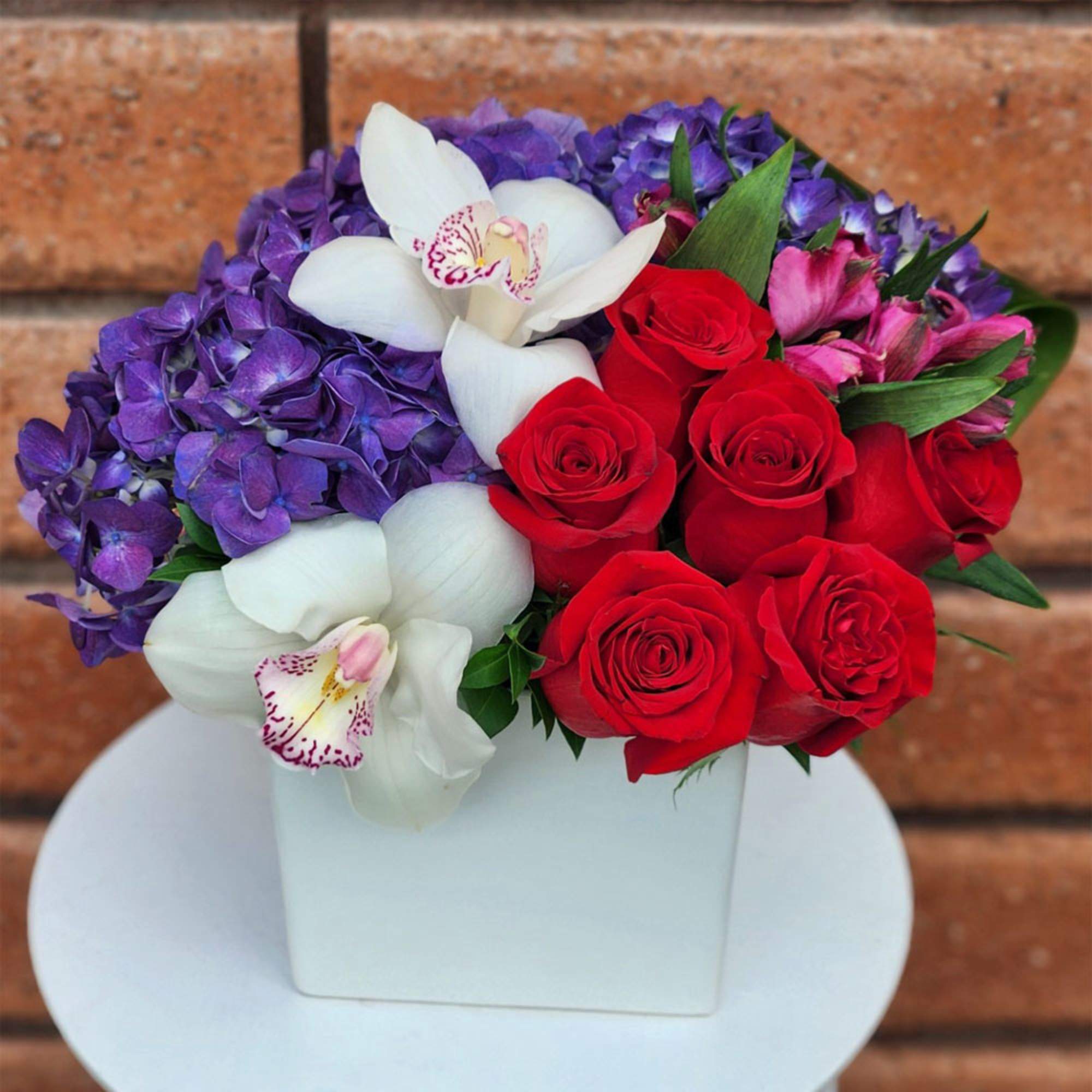 Red roses, white orchids, and purple hydrangeas in a white box