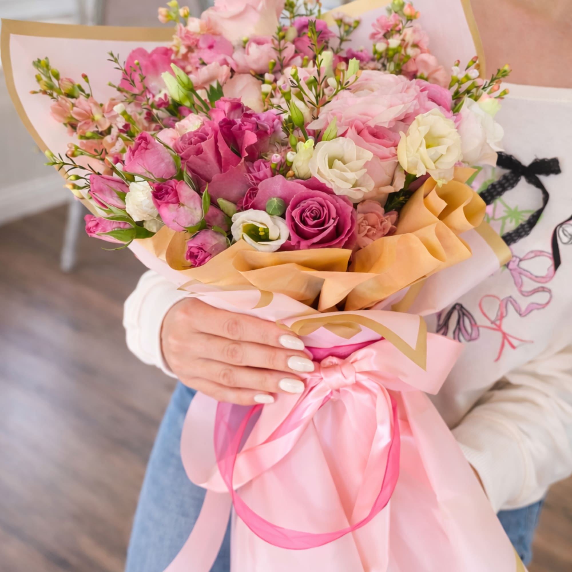 Handheld bouquet of pink and white flowers wrapped in pink paper with ribbon