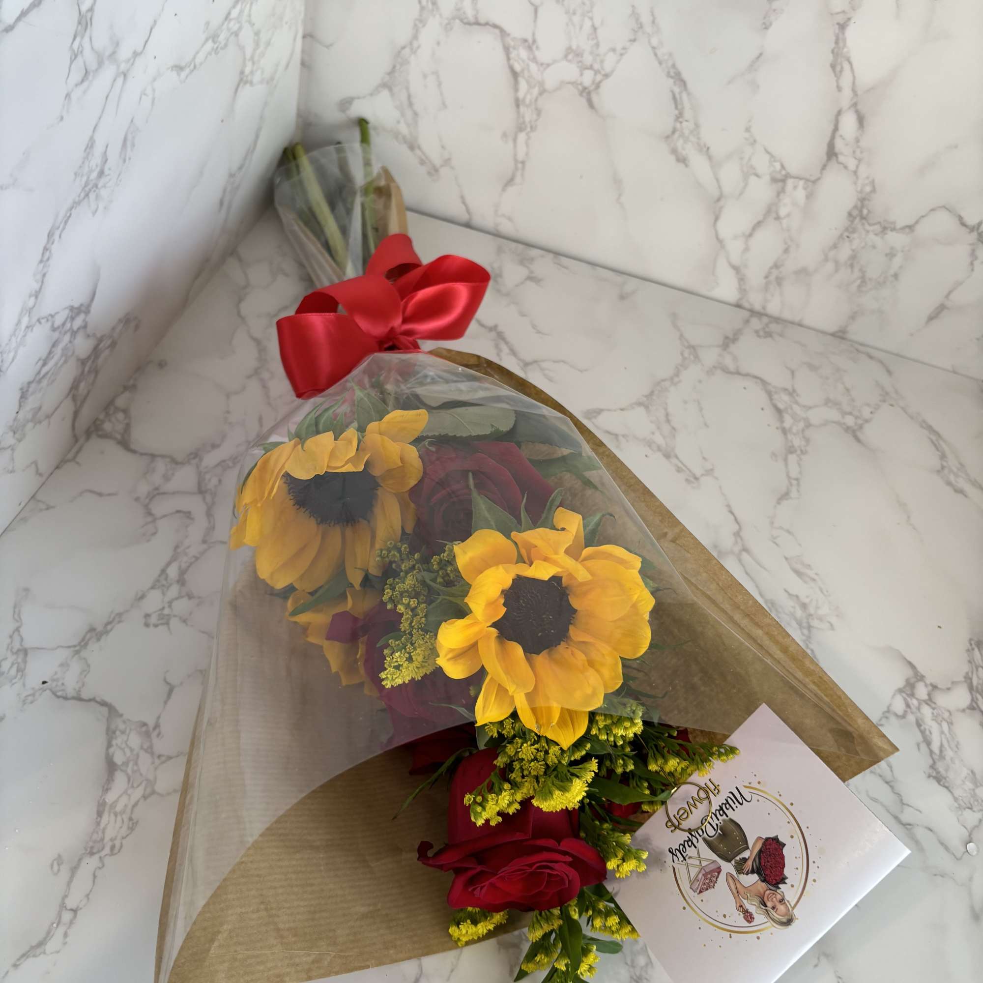 Bouquet of yellow sunflowers and red roses wrapped in paper with a red bow