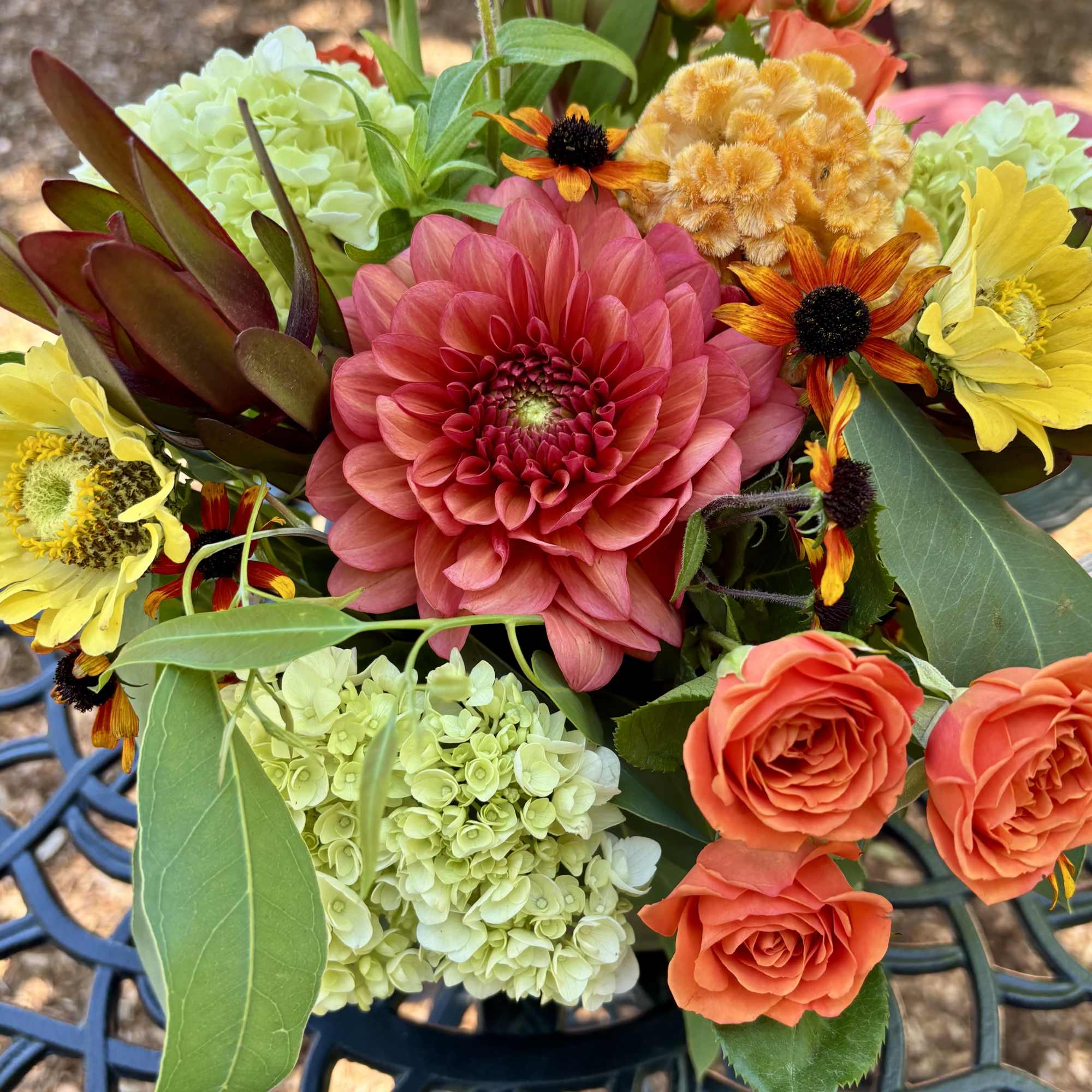 Mixed bouquet with a large pink dahlia, orange roses, and pale green hydrangeas