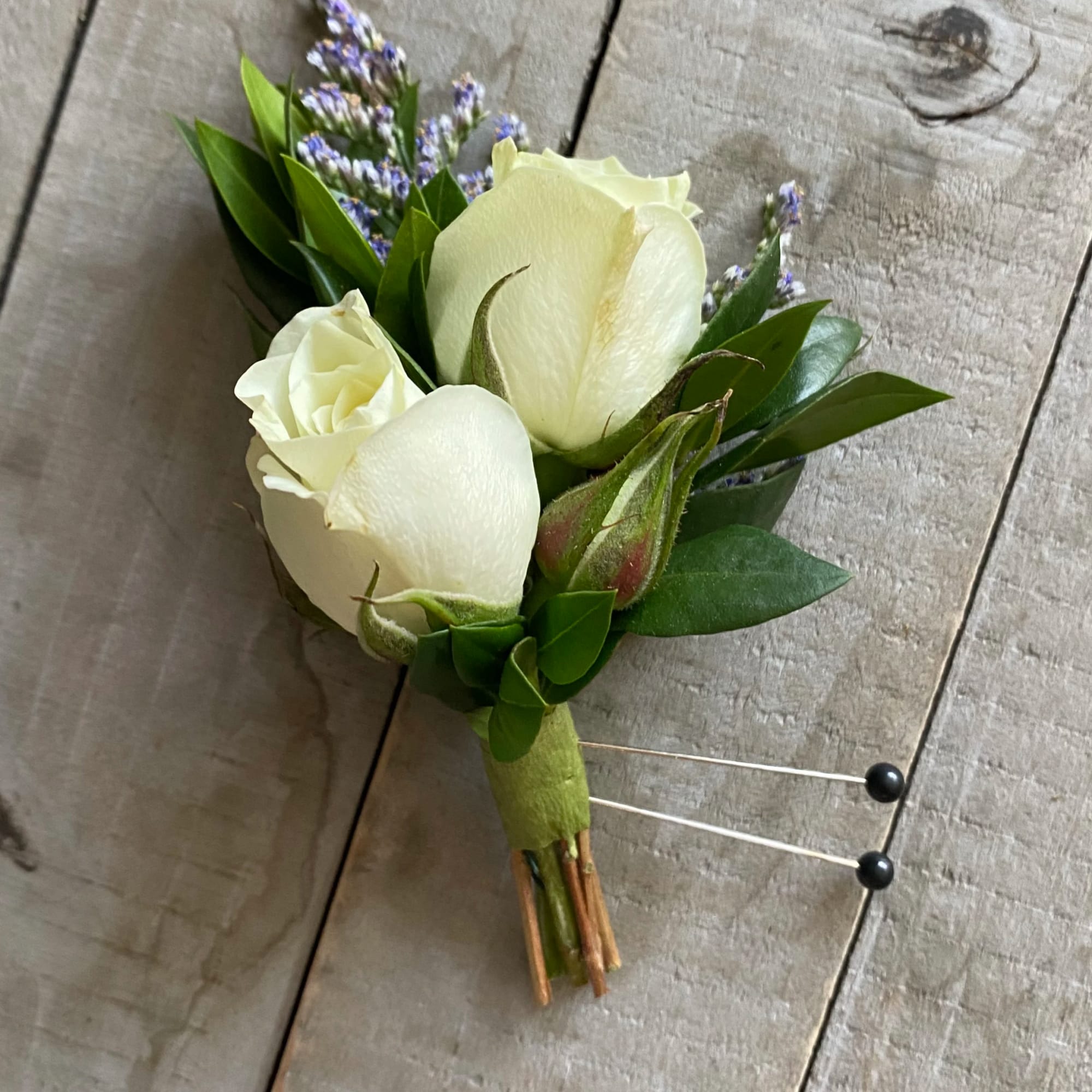 White rose boutonniere with purple filler flowers and green leaves