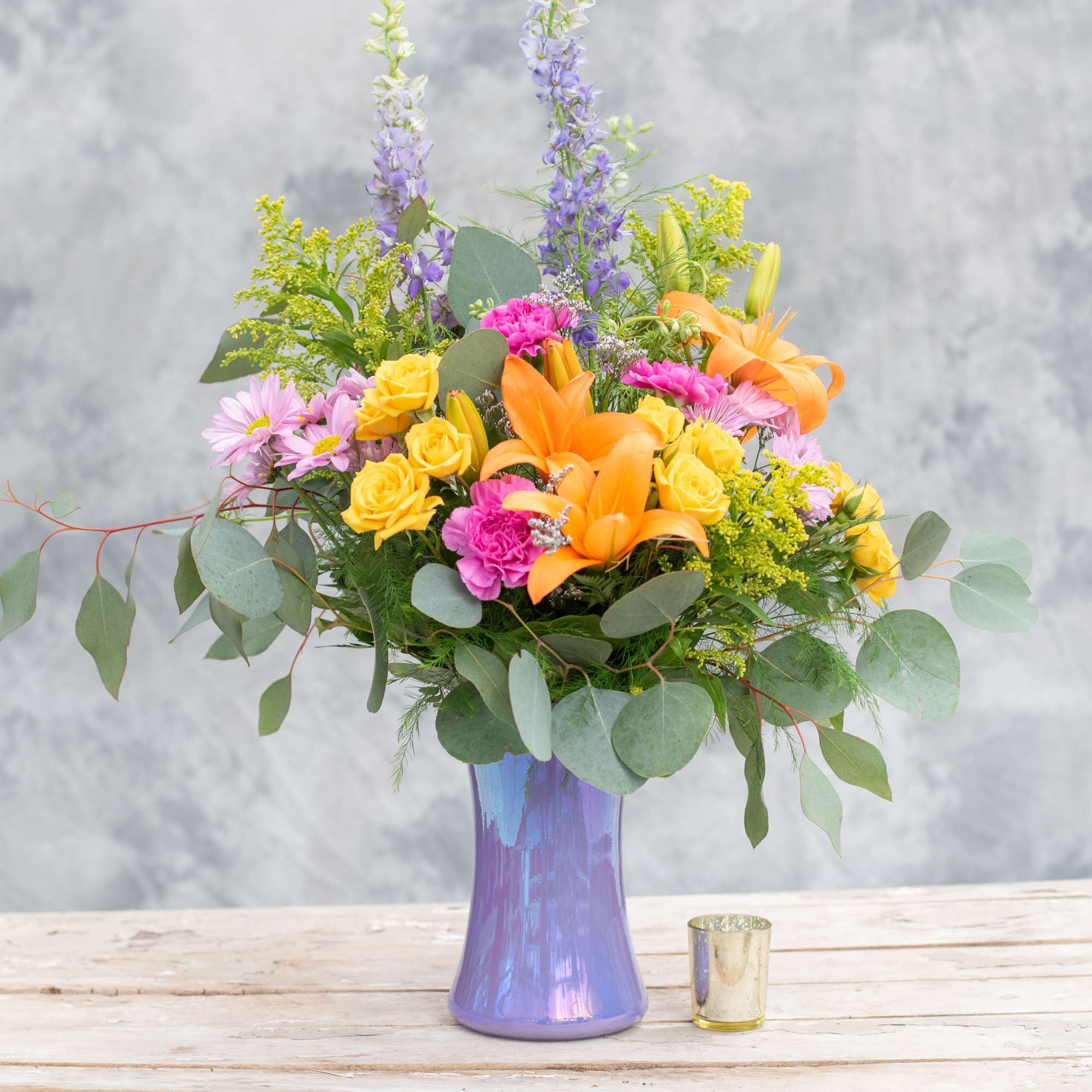 Tall iridescent lilac gathering glass vase bursting with lilies, spray roses, carnations