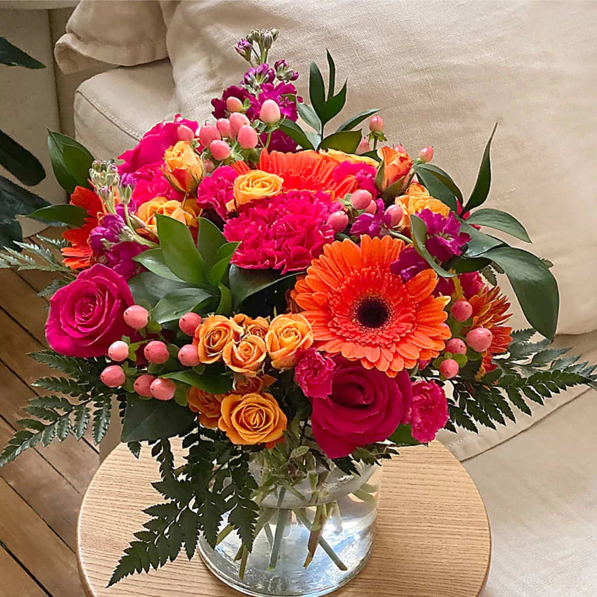 Bright bouquet of hot pink roses, orange gerbera daisies, and yellow spray roses in a clear glass vase.