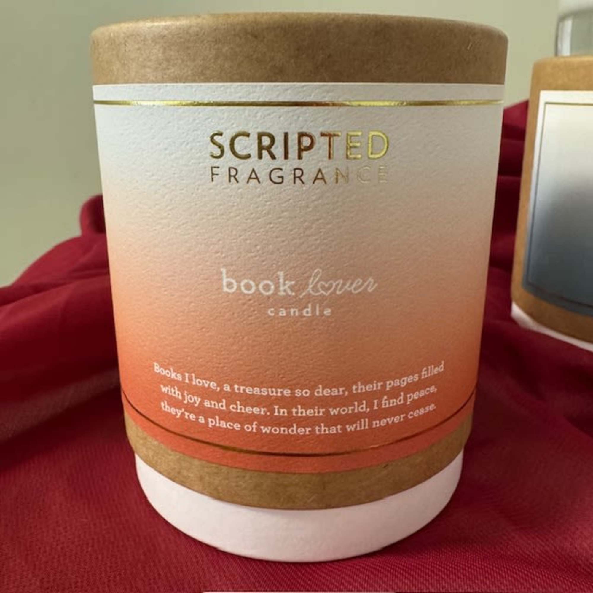 A scented candle in a tan and white container with gold lettering