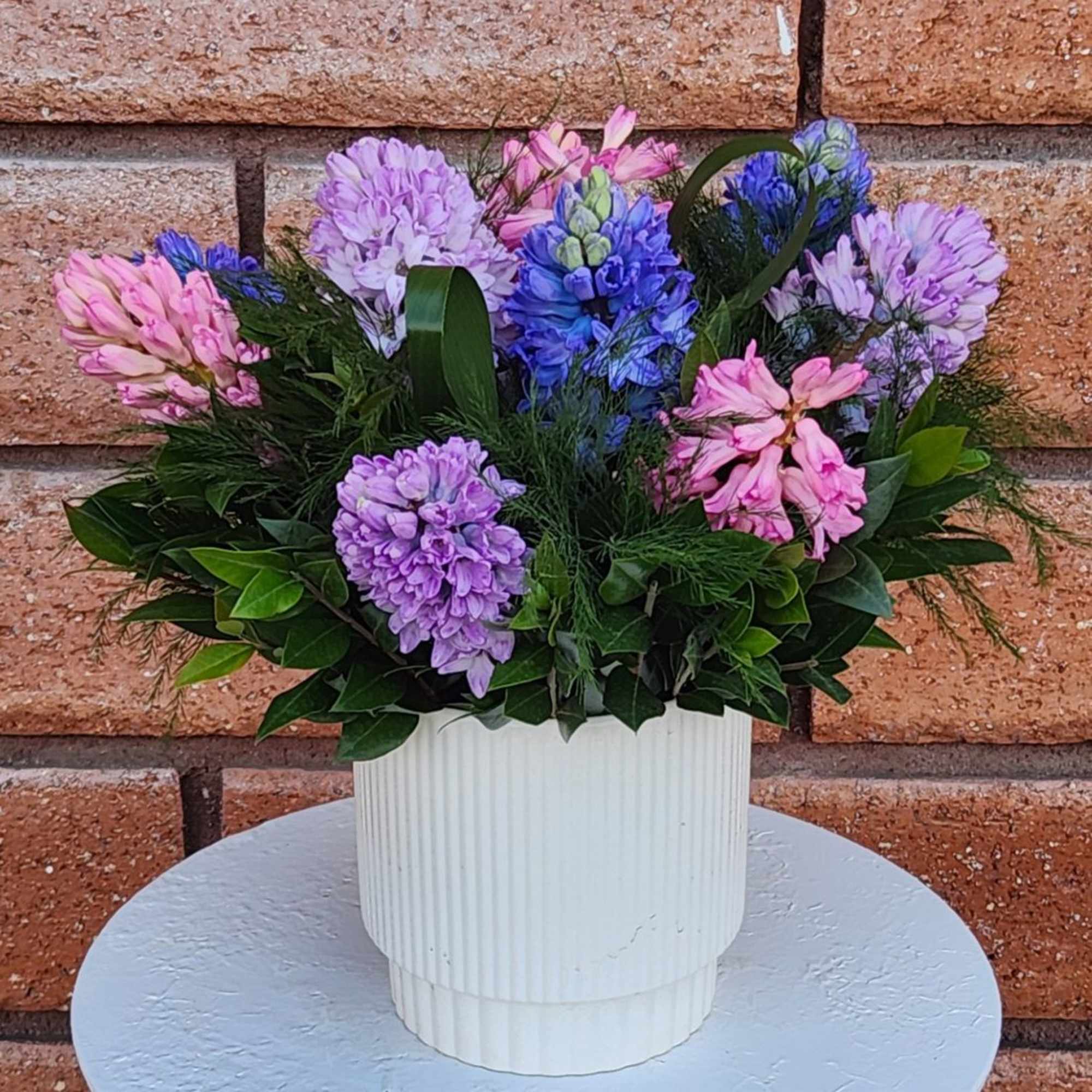 Pastel pink, purple, and blue hyacinths arranged in a white ribbed pot
