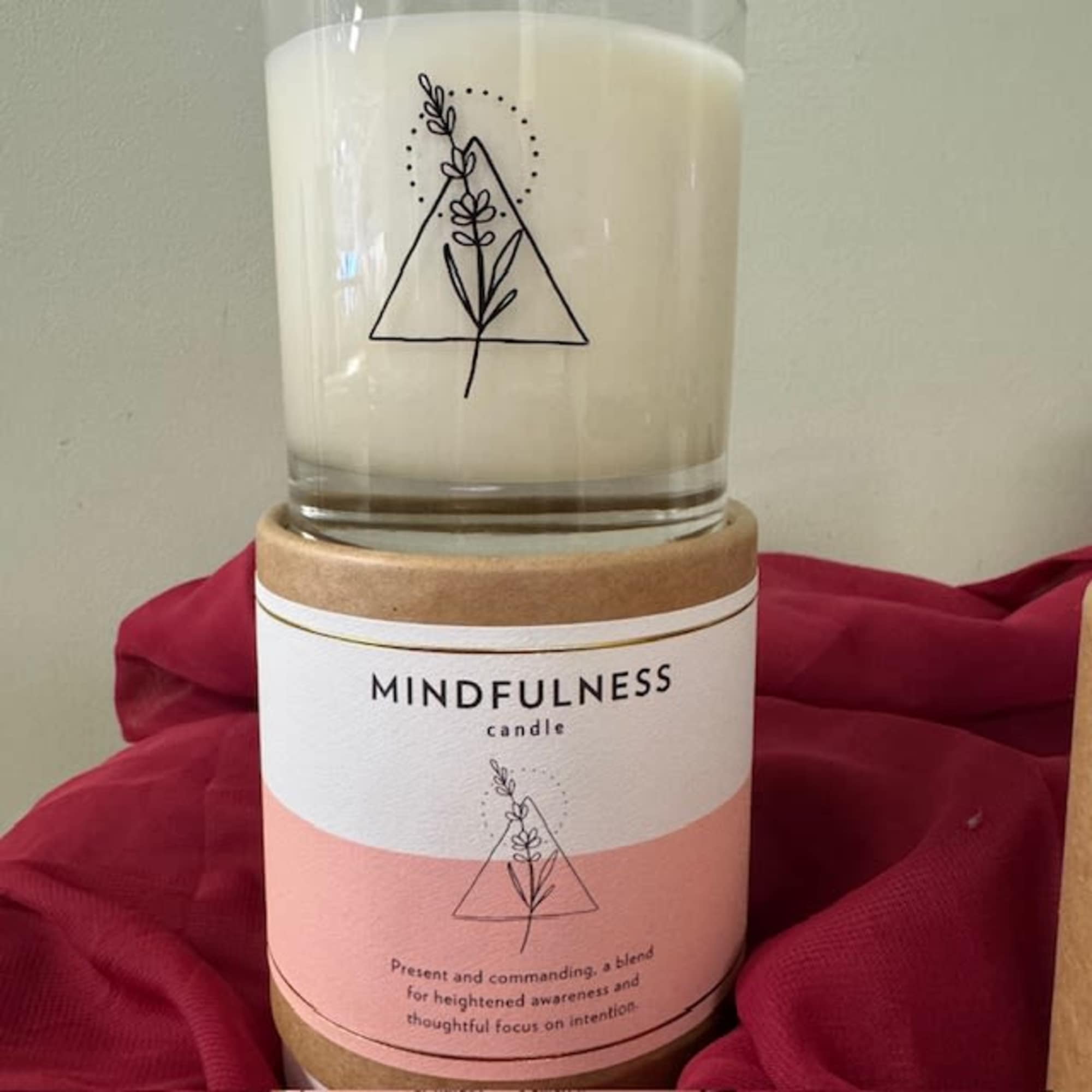 White candle in a glass jar with a pink label and kraft lid