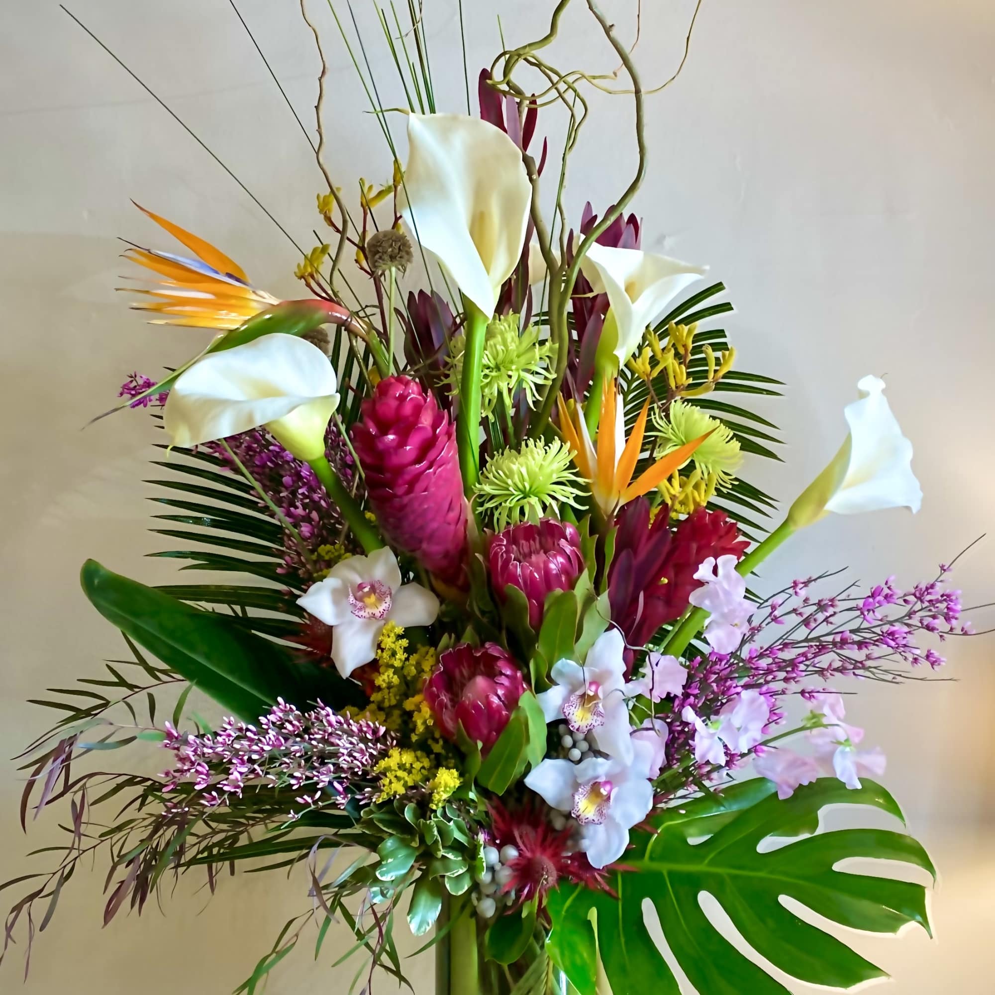 Tall tropical bouquet with white calla lilies and pink blooms in a glass vase