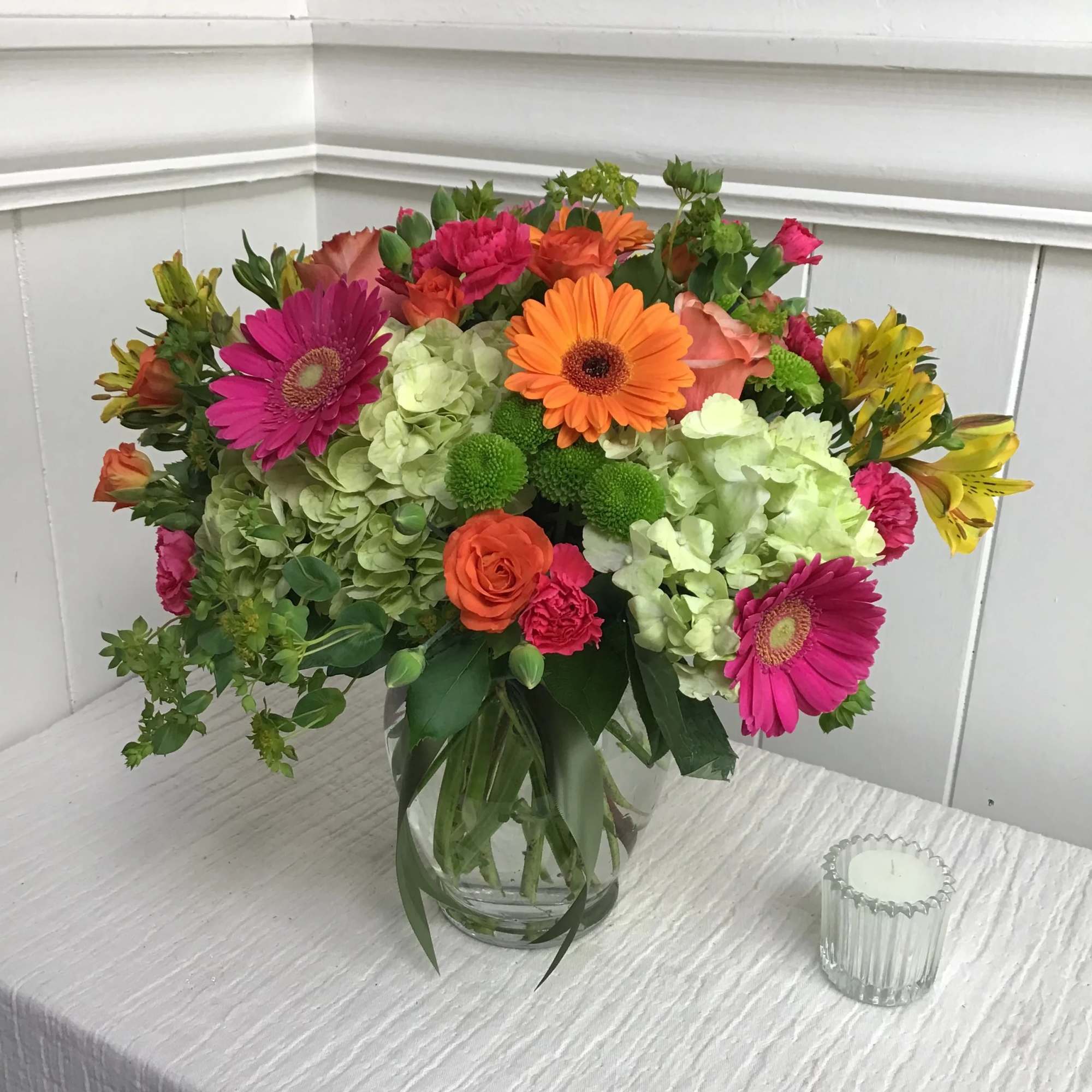 Bright mixed bouquet of gerbera daisies, roses, and hydrangeas in a clear glass vase