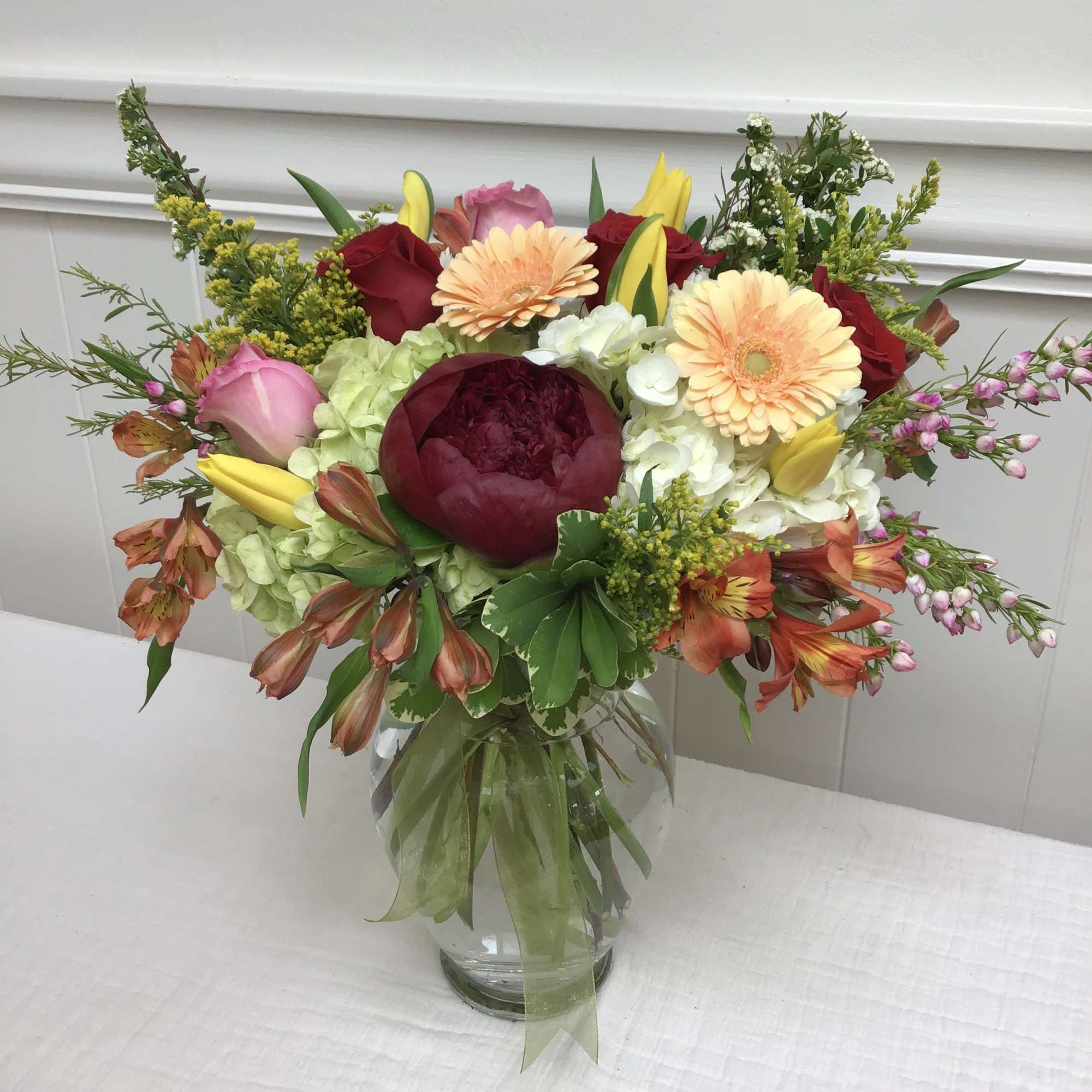 Mixed bouquet with red peony, roses, peach gerberas and yellow lilies in a clear glass vase