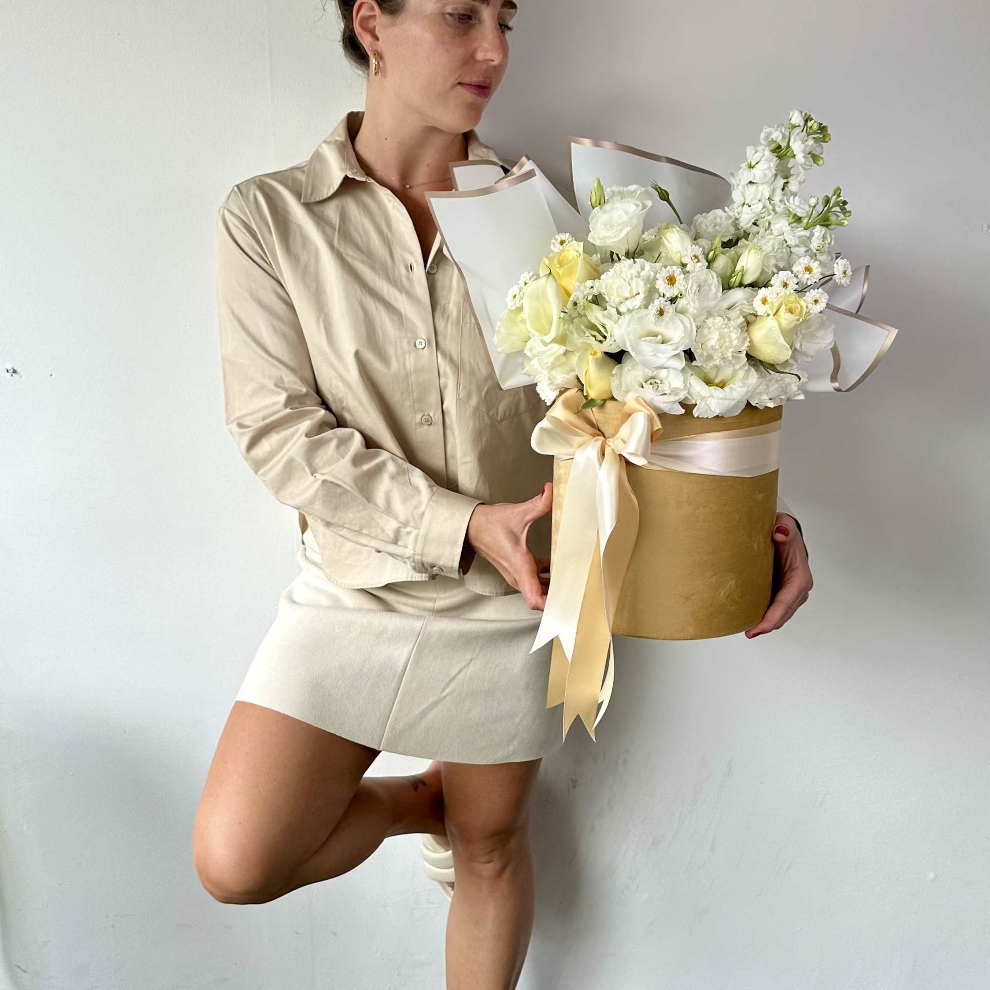 Woman holding a white and pale yellow flower arrangement in a gold box