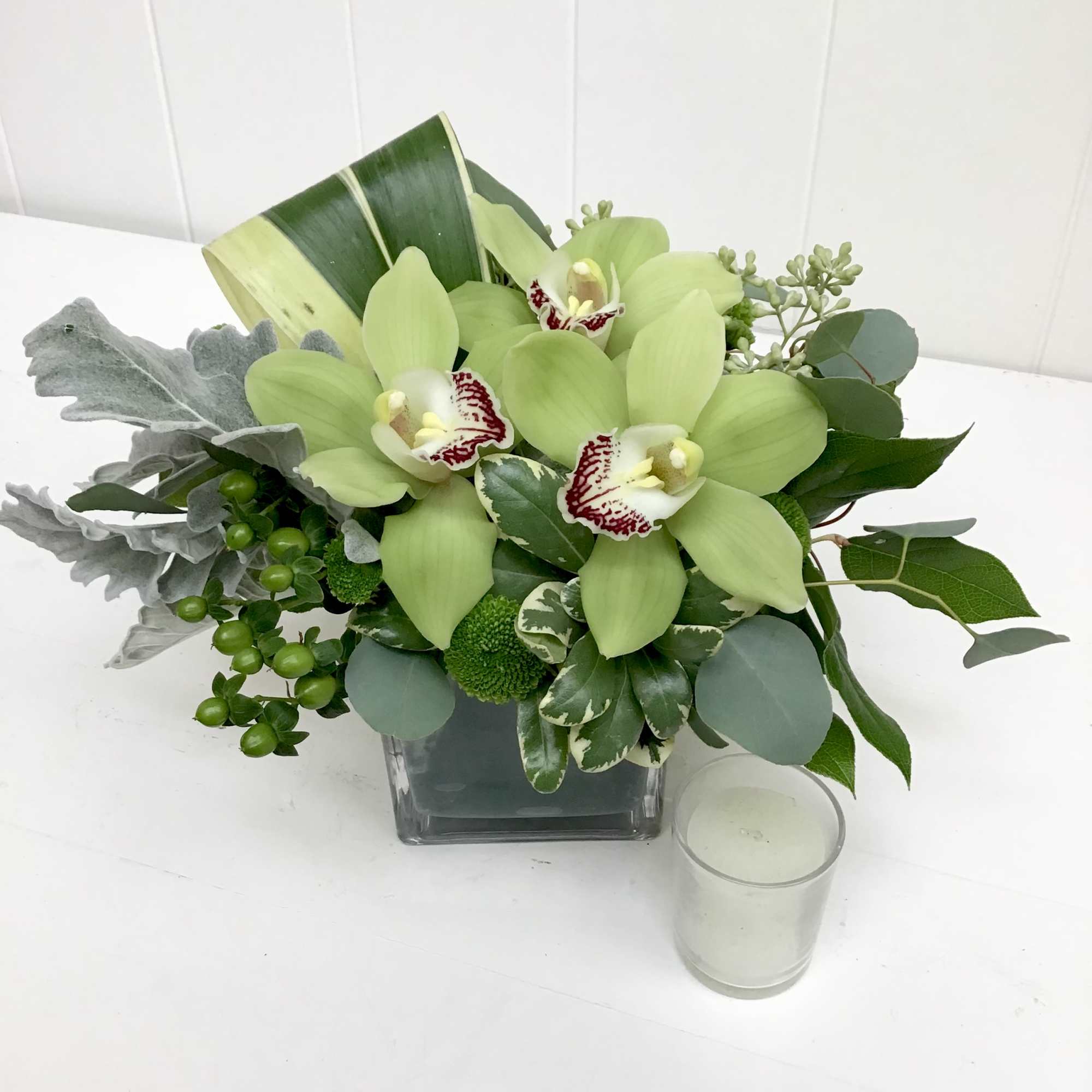 Green orchid arrangement in a square glass vase with a small candle