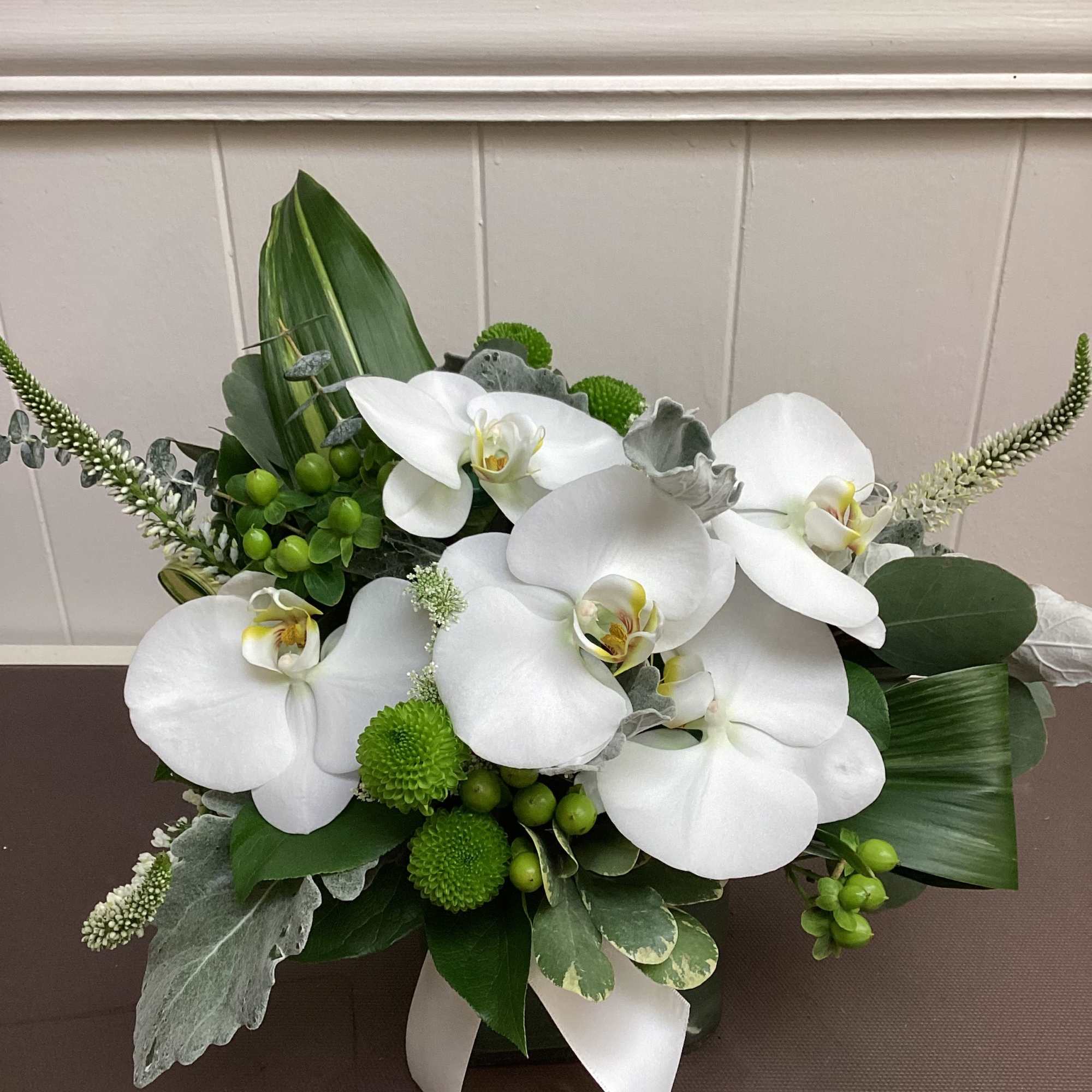 White orchids arranged with green accents in a low container