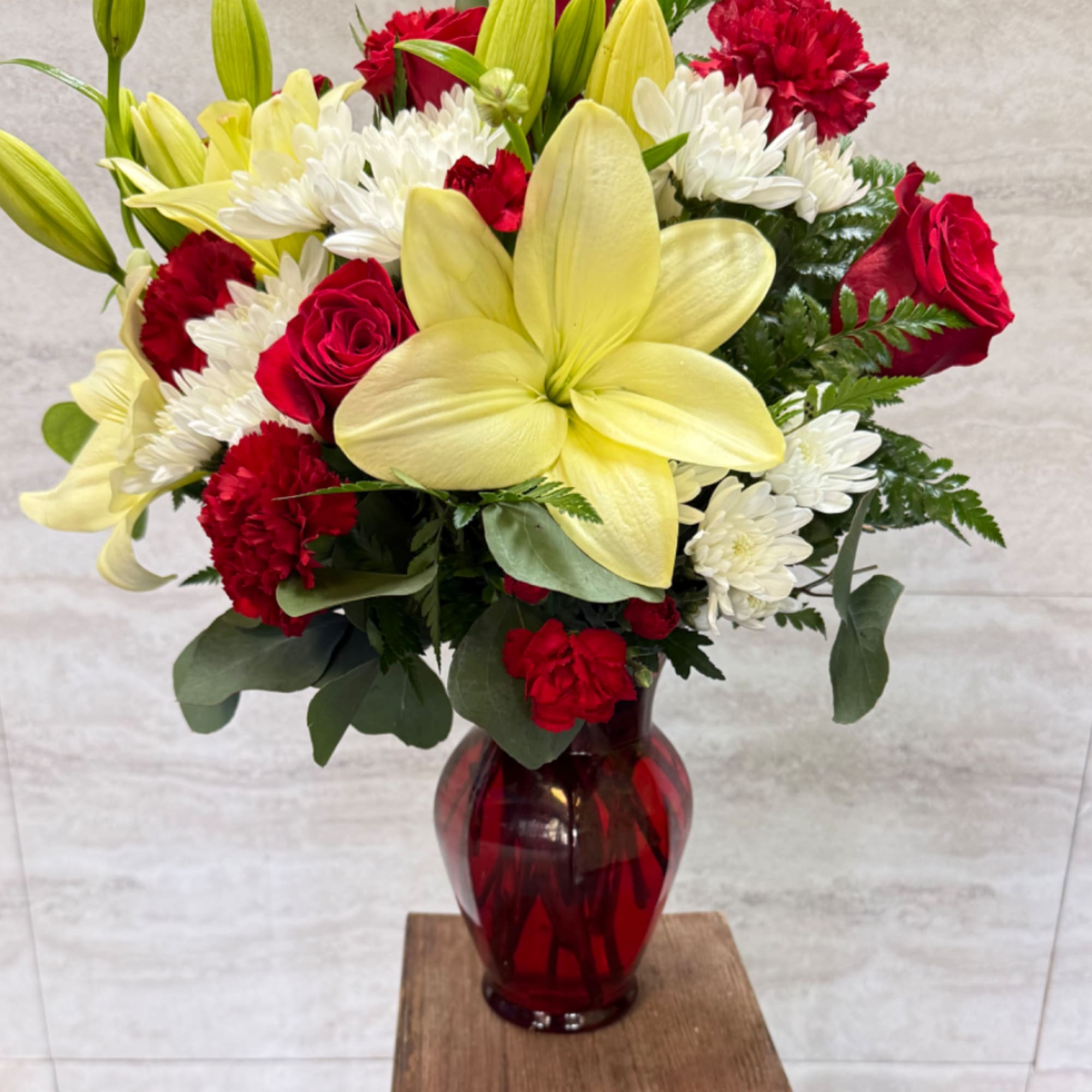 Bouquet of red roses, white chrysanthemums, and yellow lilies in a red glass vase