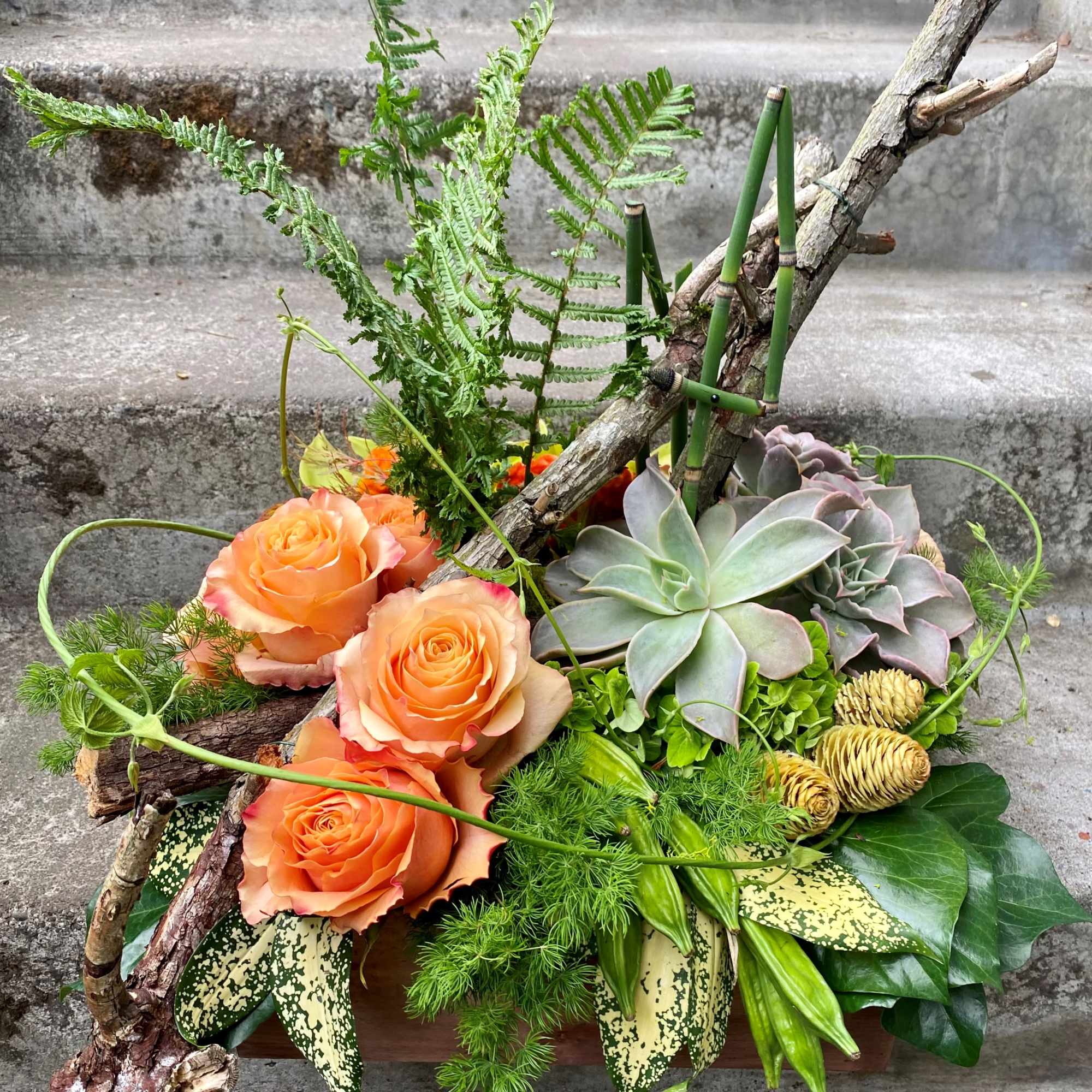 Orange roses and succulents arranged with branches in a wooden container