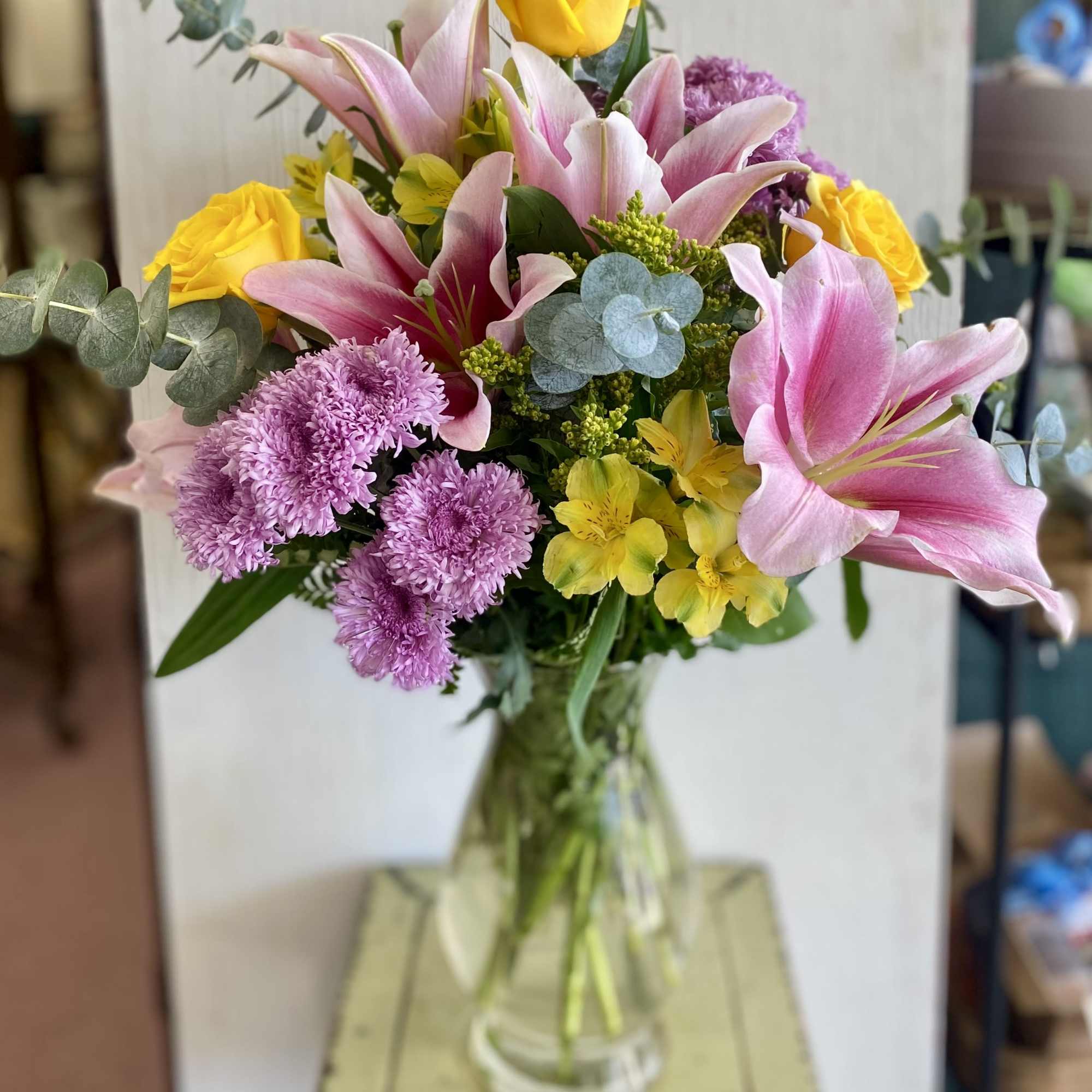 Bouquet of pink lilies, yellow roses, and purple flowers in a glass vase