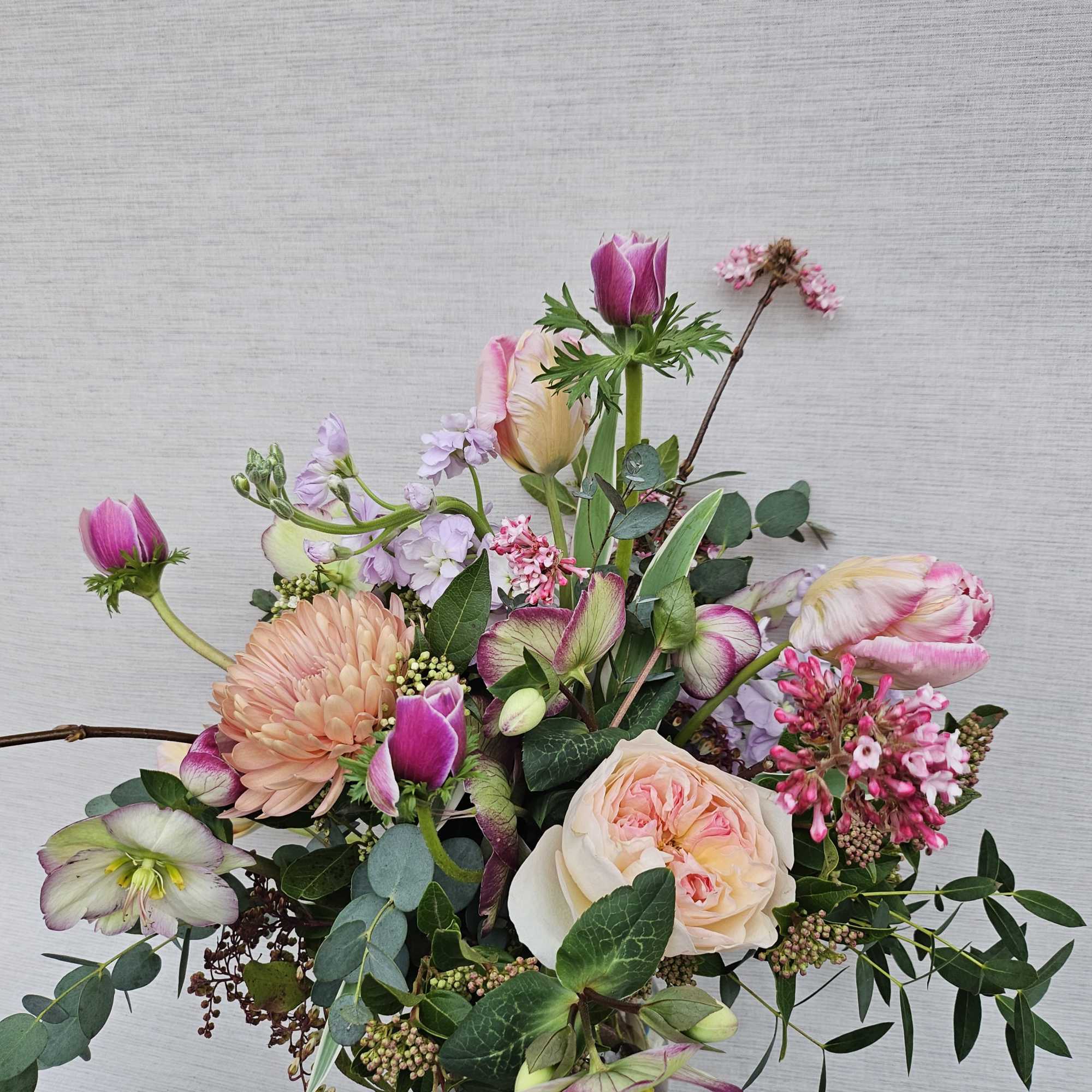 Loose arrangement of pink and peach blooms, including roses and tulips, in a clear glass vase