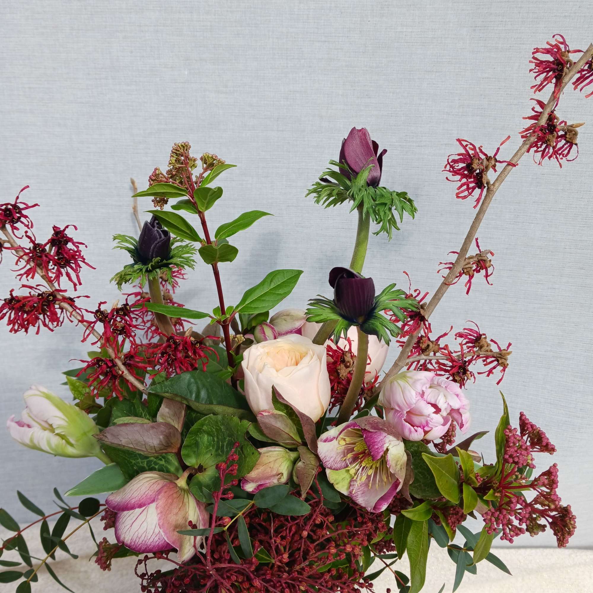 Loose arrangement of blush roses, pink peonies, and dark purple blooms in a clear glass vase