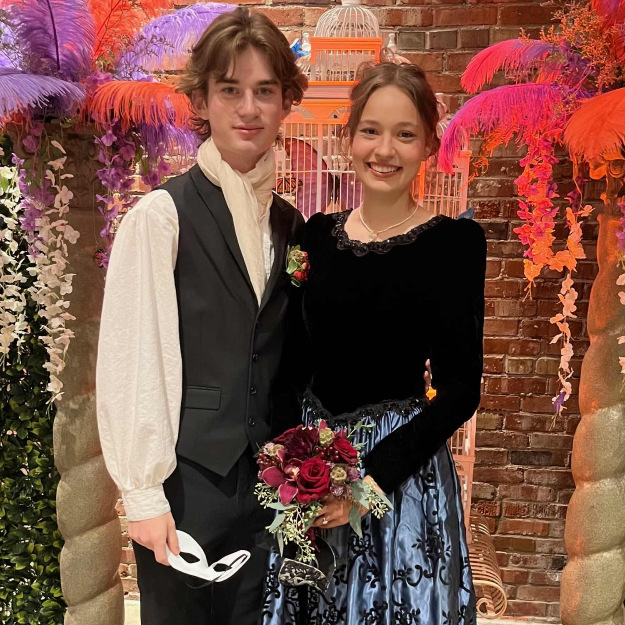 Young couple posing with a small red rose bouquet at a formal event