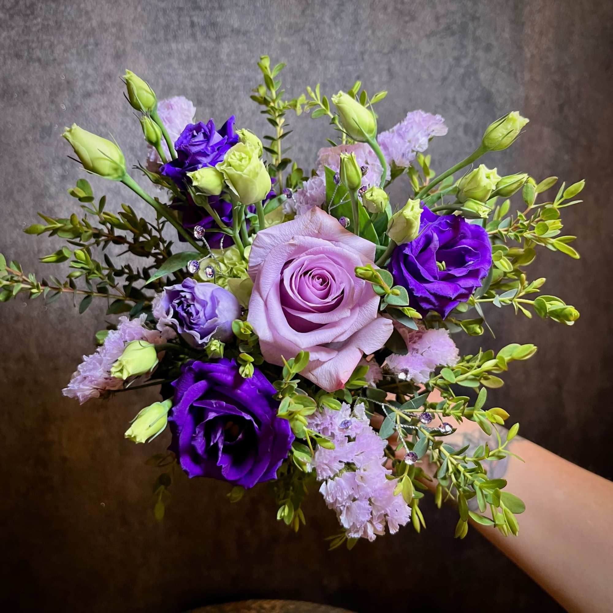Handheld bouquet of lavender and purple roses with small pink filler flowers