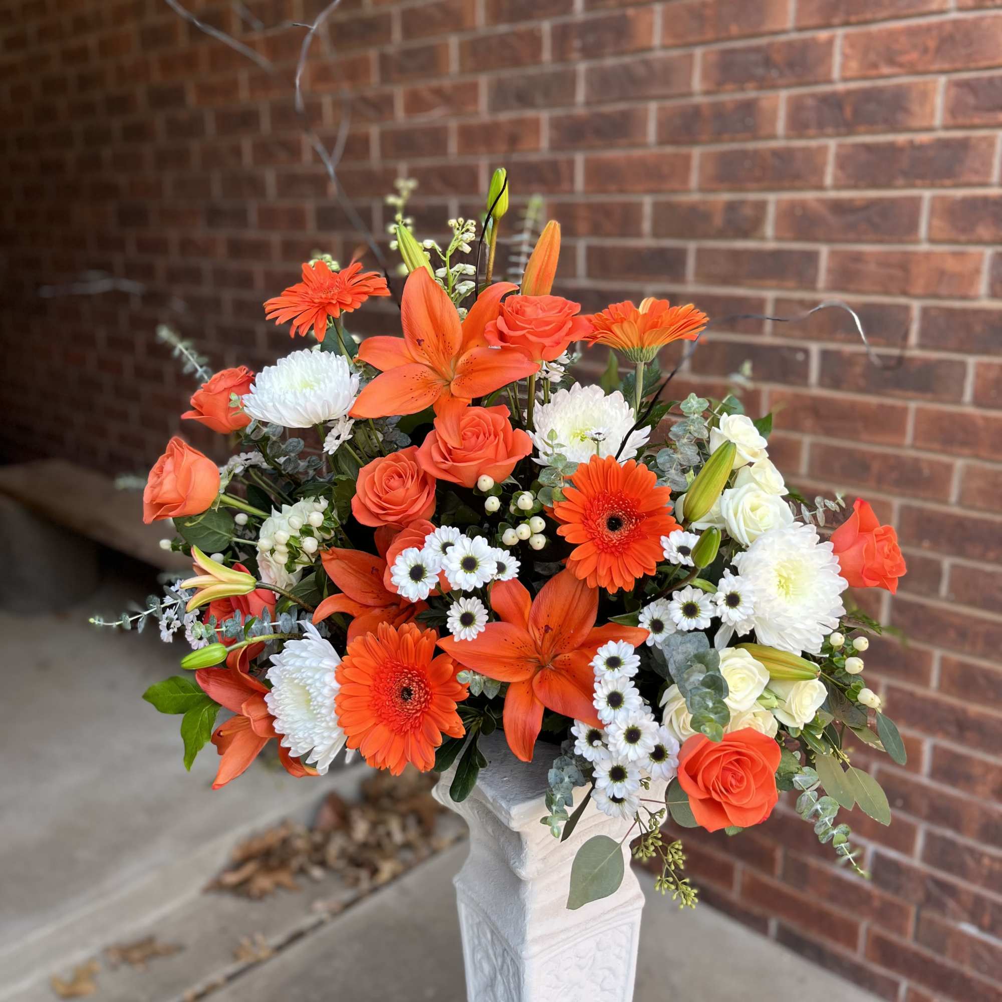 Bright, energetic orange roses, lilies, and gerbera daisies mingle with crisp white