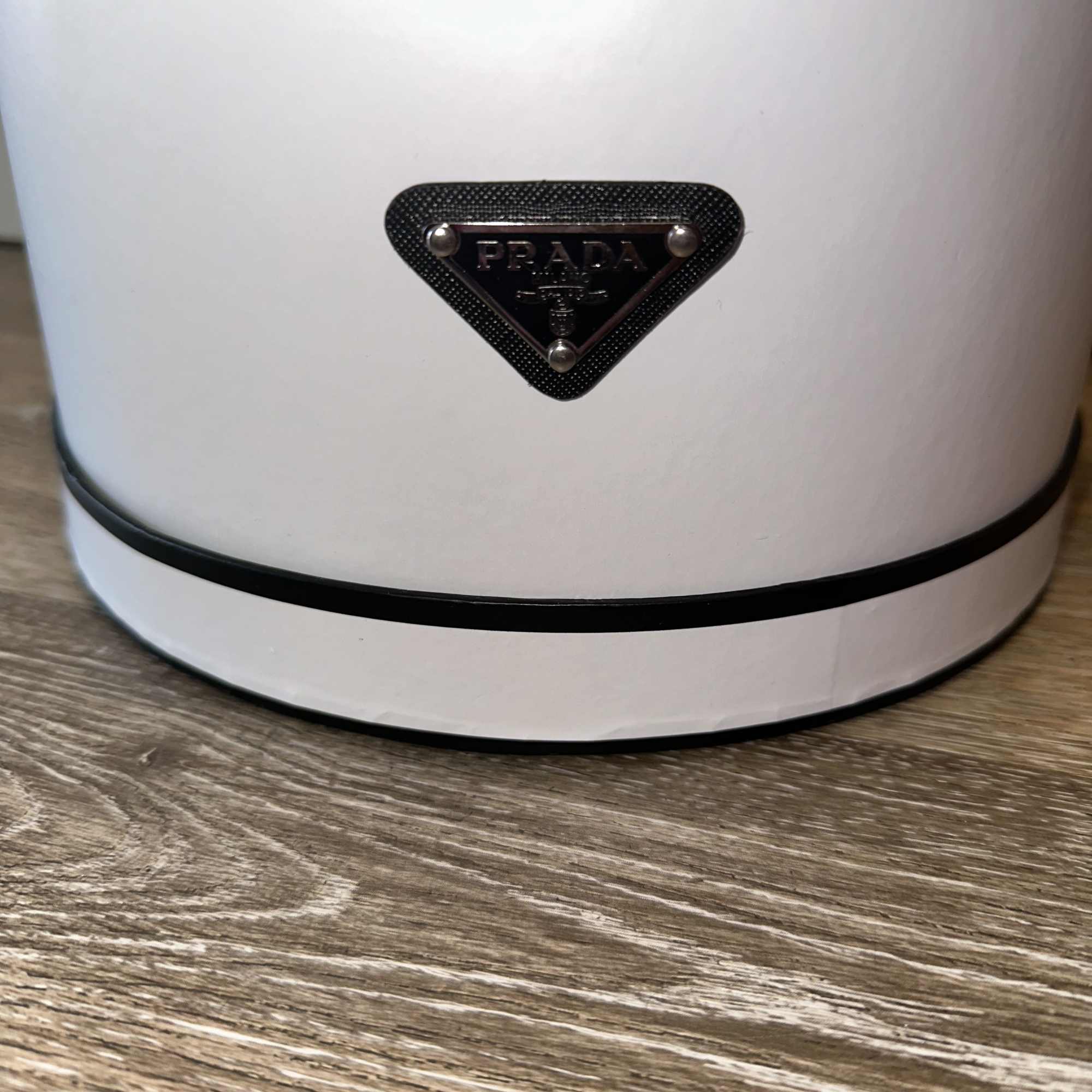 White Prada container with a black logo plaque on a wood surface