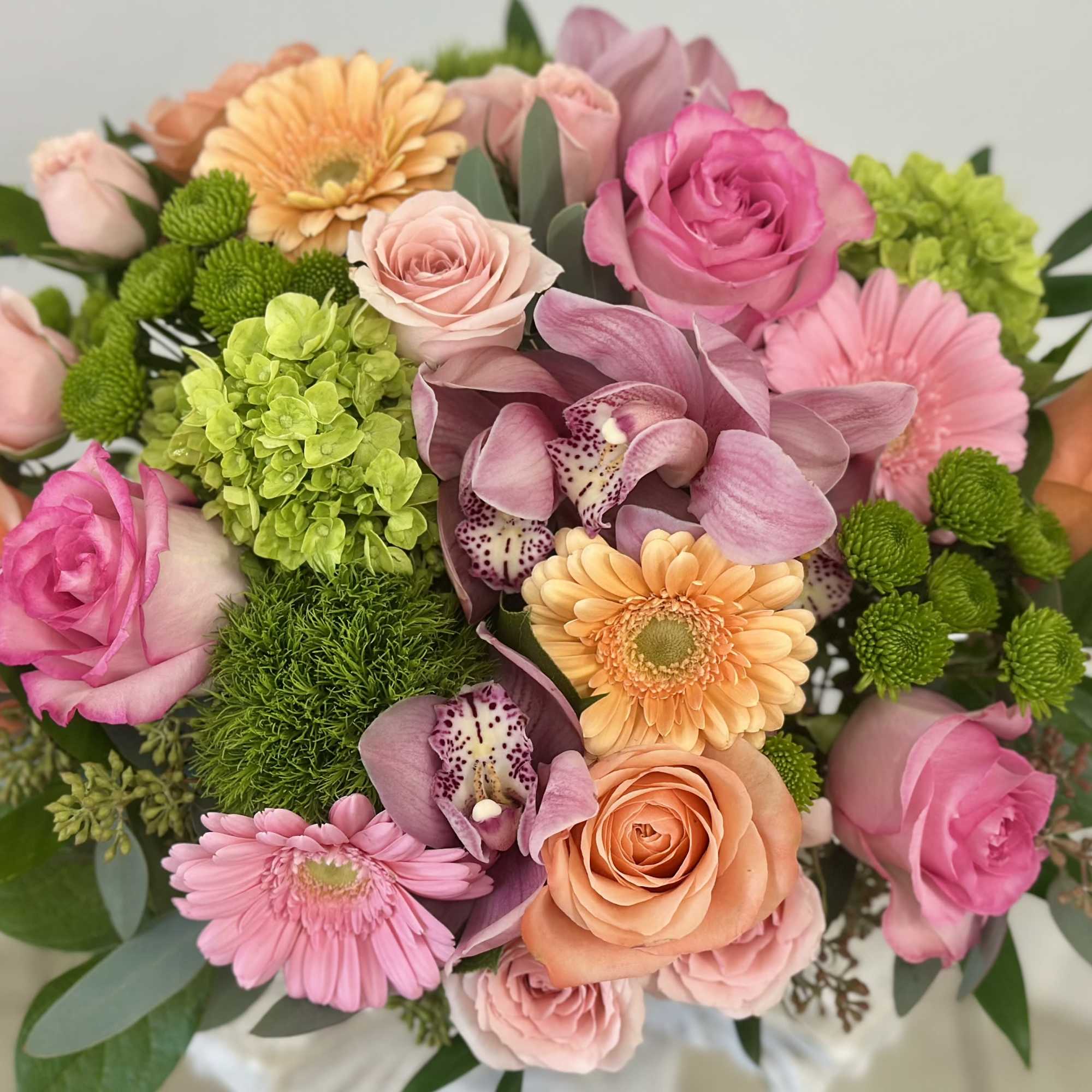 Round bouquet of pink roses, peach gerberas, green hydrangea, and mauve orchids