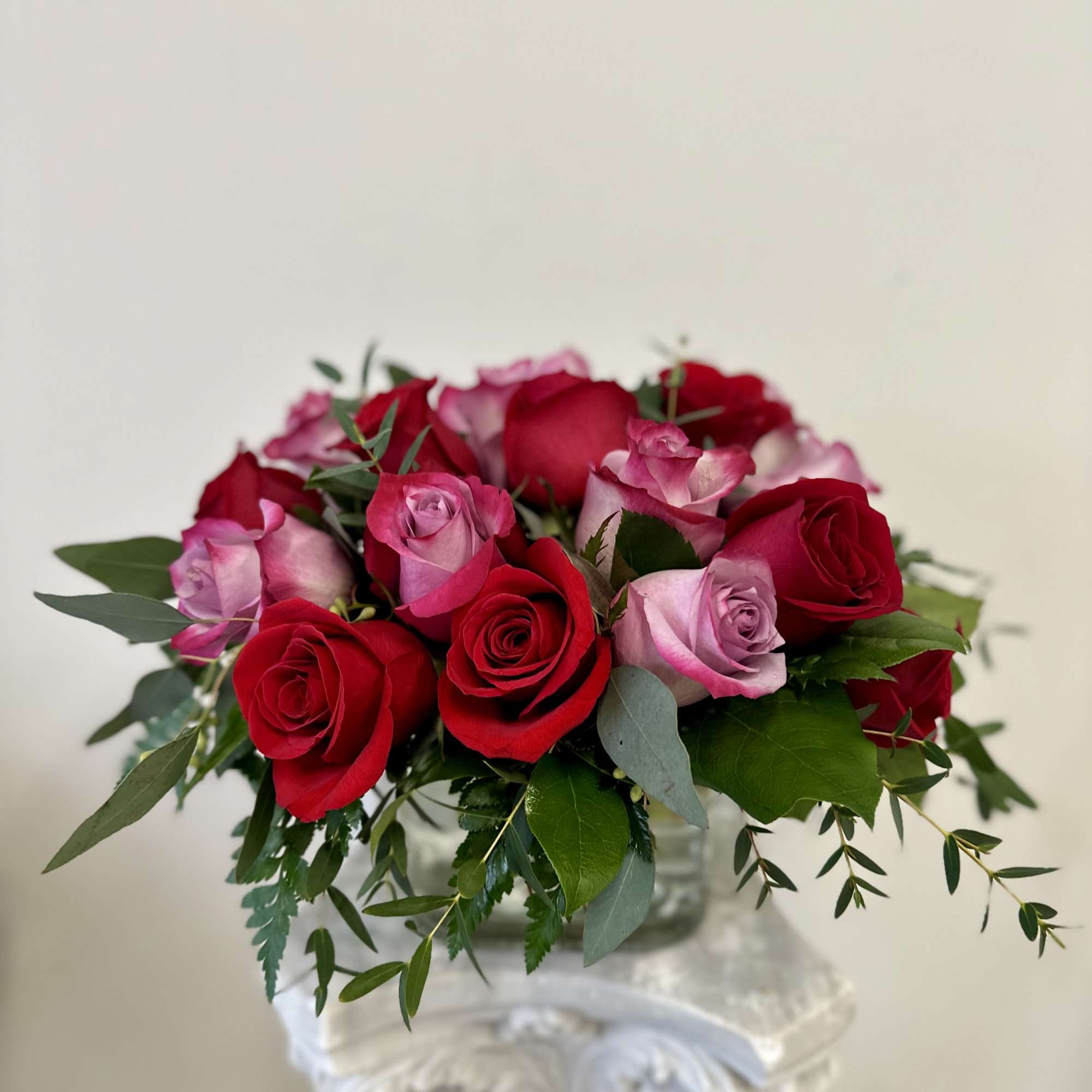 Bouquet of red and pink roses with greenery in a clear vase