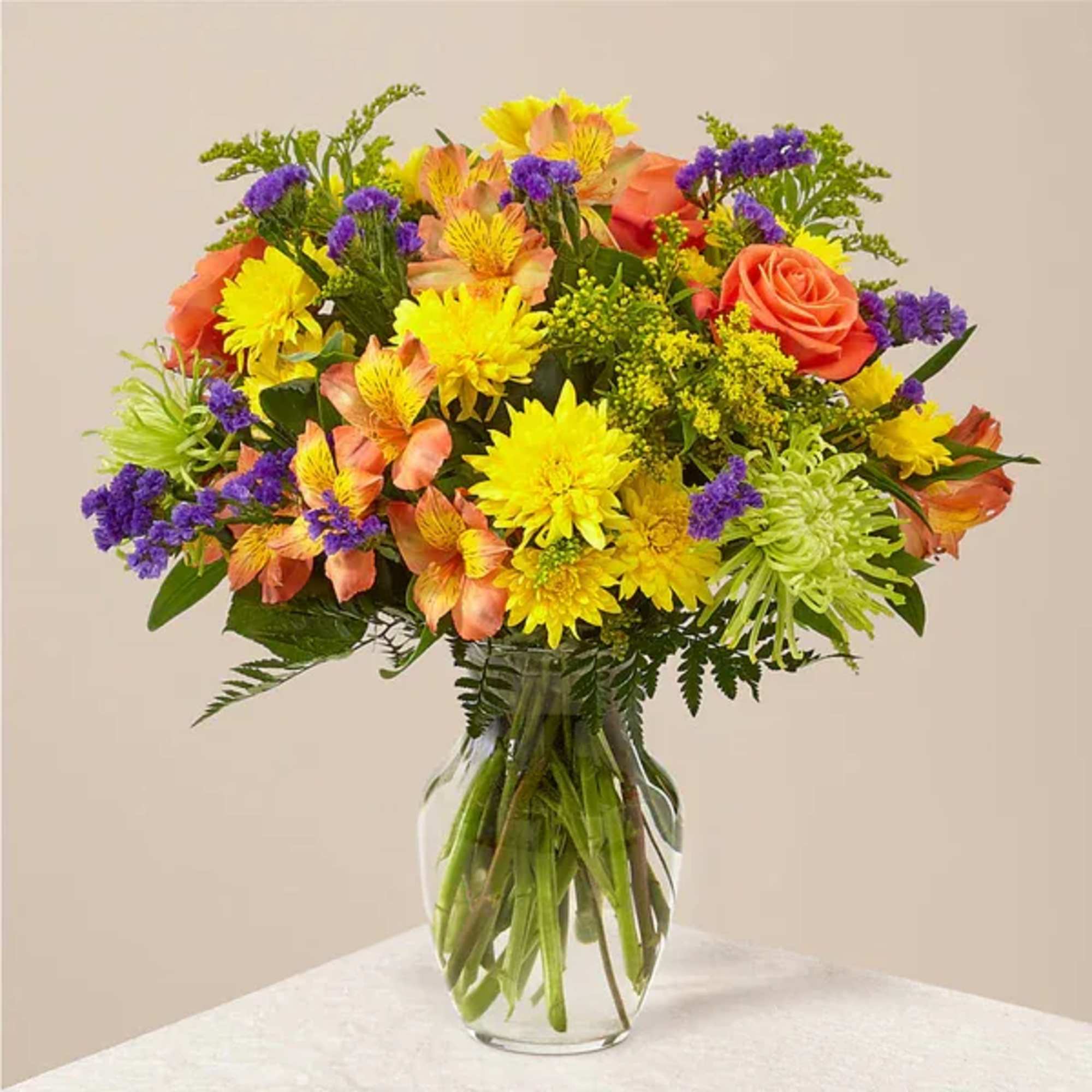 Mixed bouquet of yellow, orange, and purple flowers in a glass vase