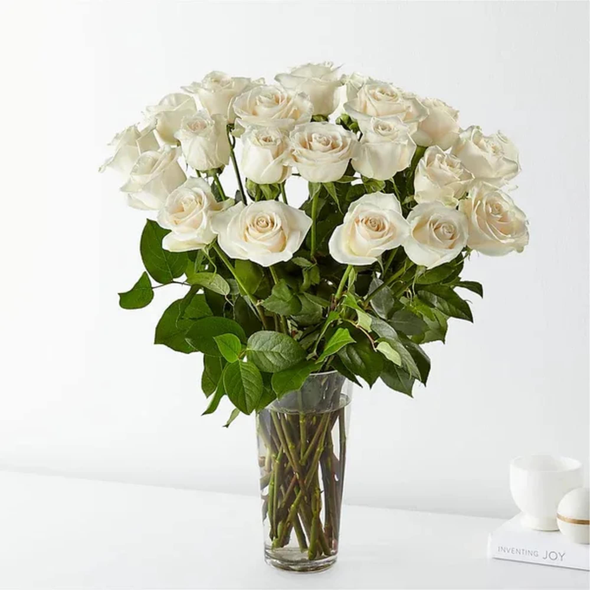 White roses arranged in a clear glass vase with green foliage