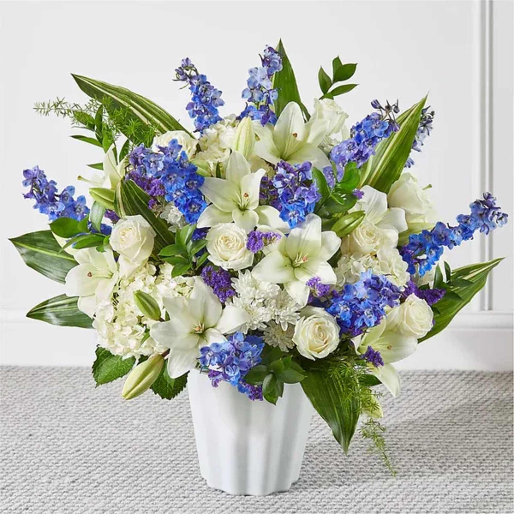 White lilies and roses with blue flowers in a white vase