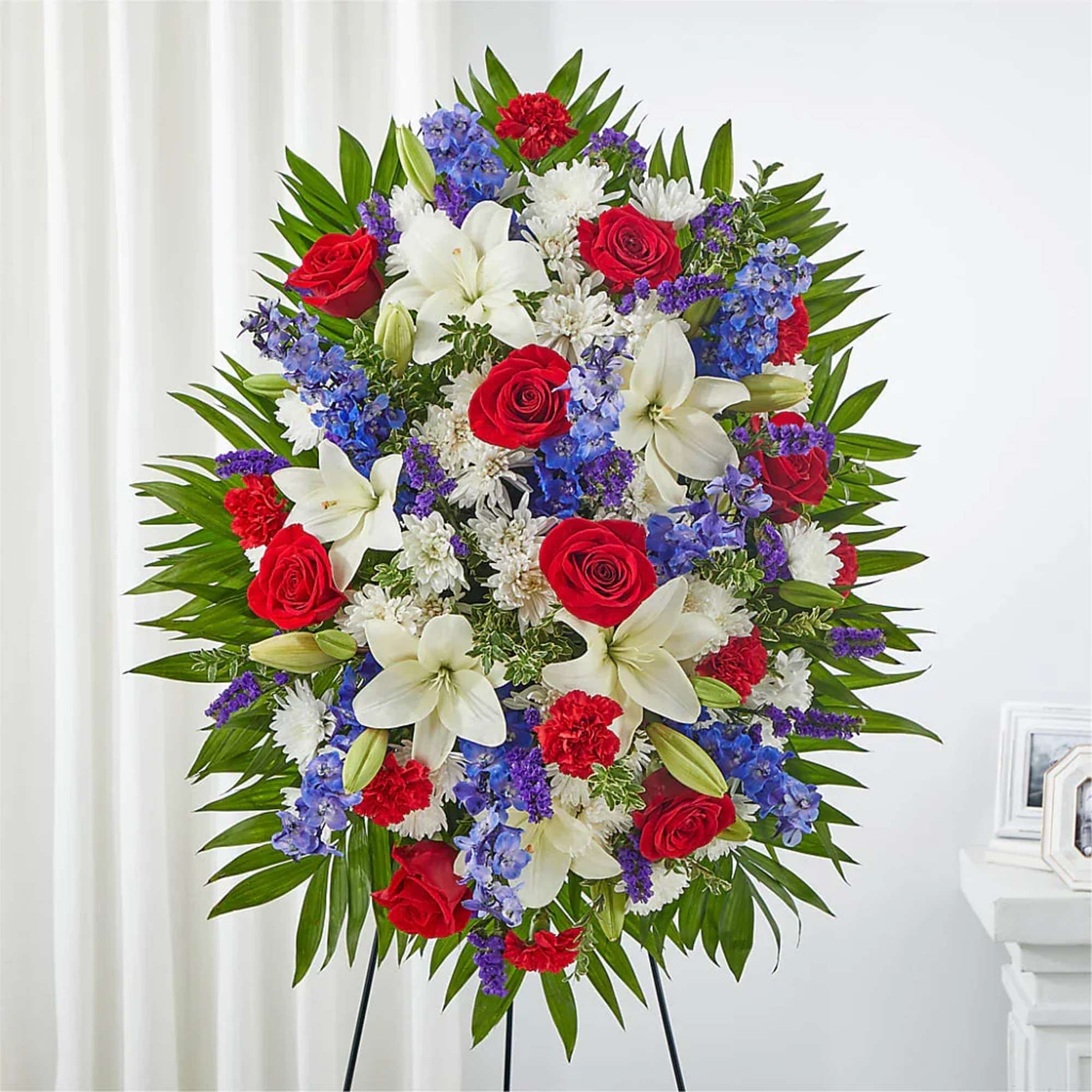 Standing floral wreath with red roses, white lilies, and blue flowers