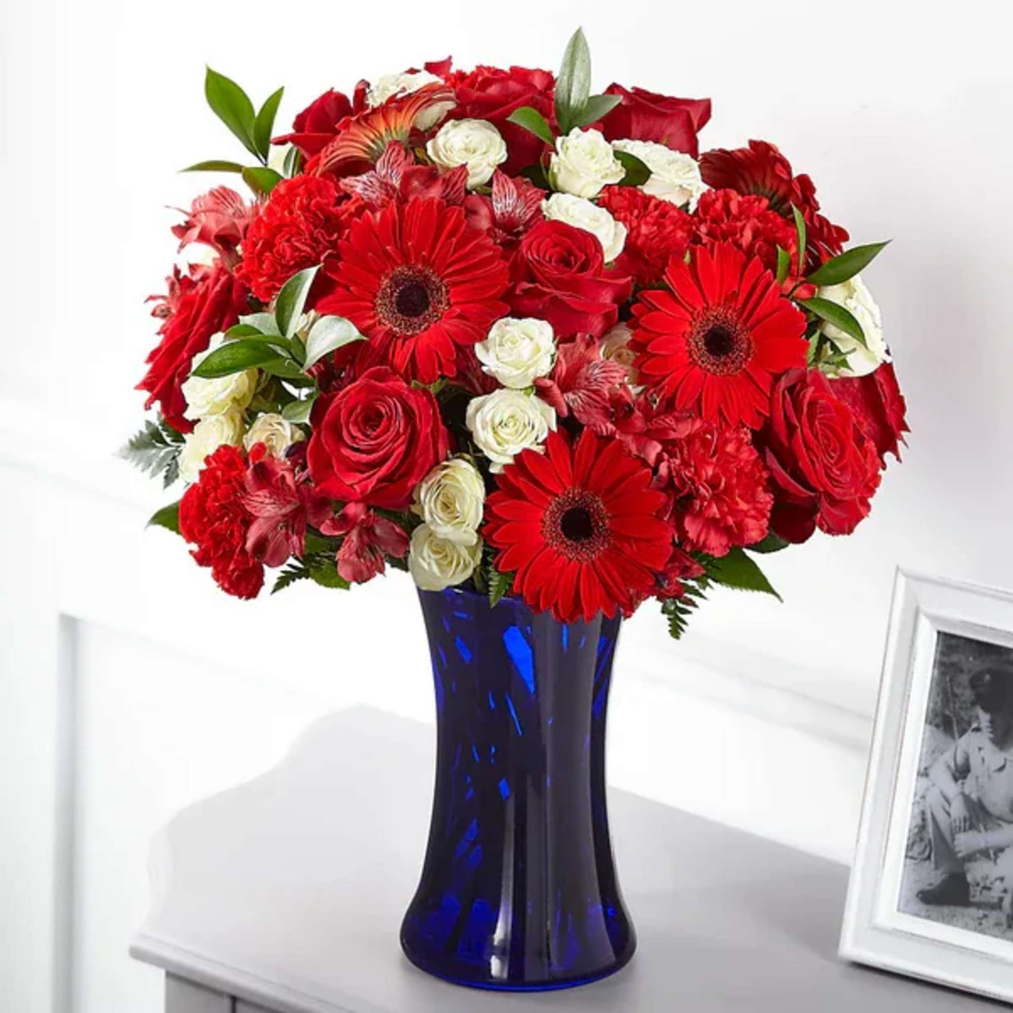 Red and white flower arrangement in a blue glass vase