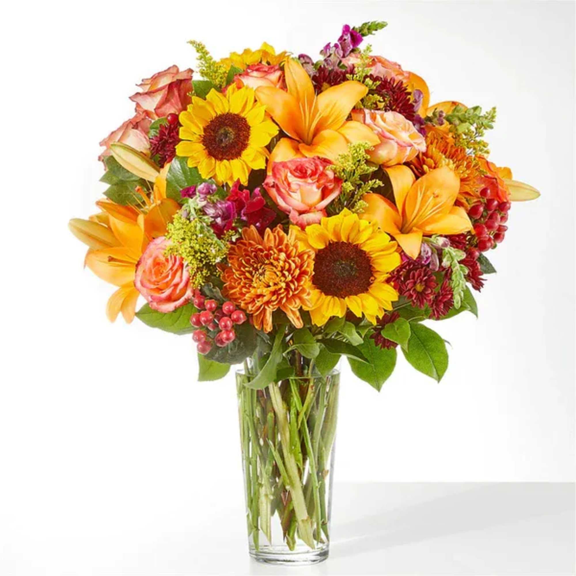Mixed bouquet of sunflowers, lilies, and roses in a clear glass vase