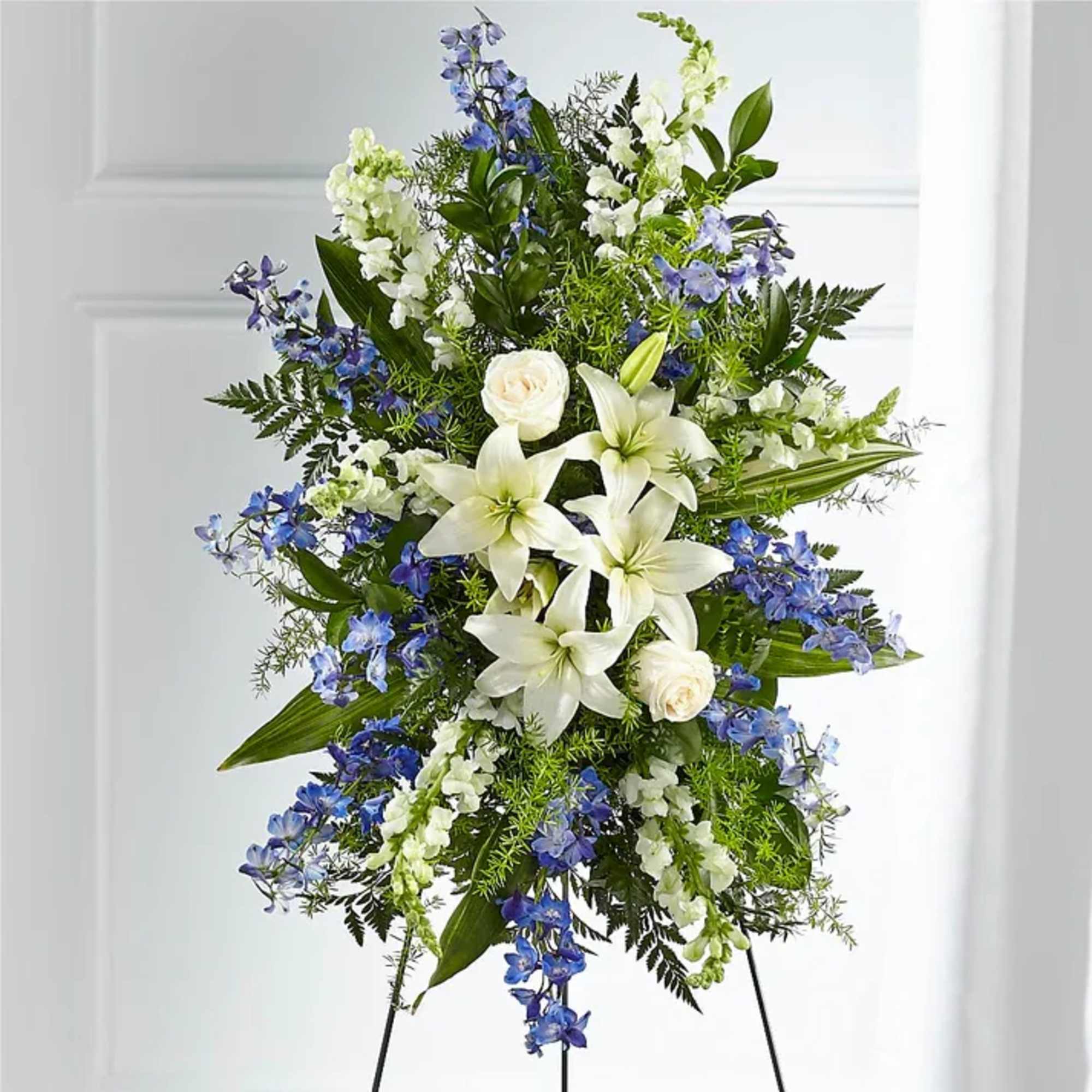 Standing floral spray with white lilies and blue flowers on a black easel