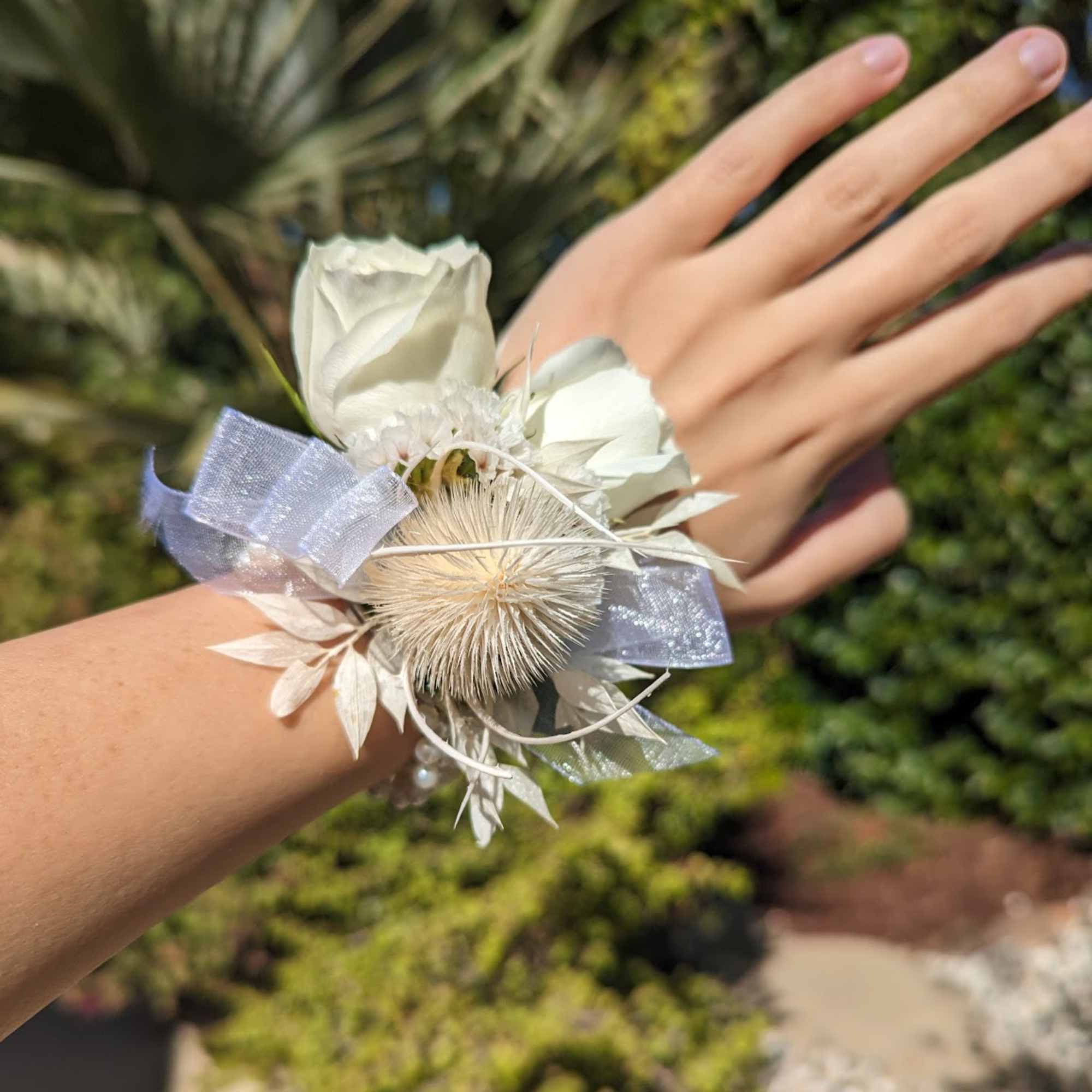 White floral wrist corsage with ribbon on a person's wrist
